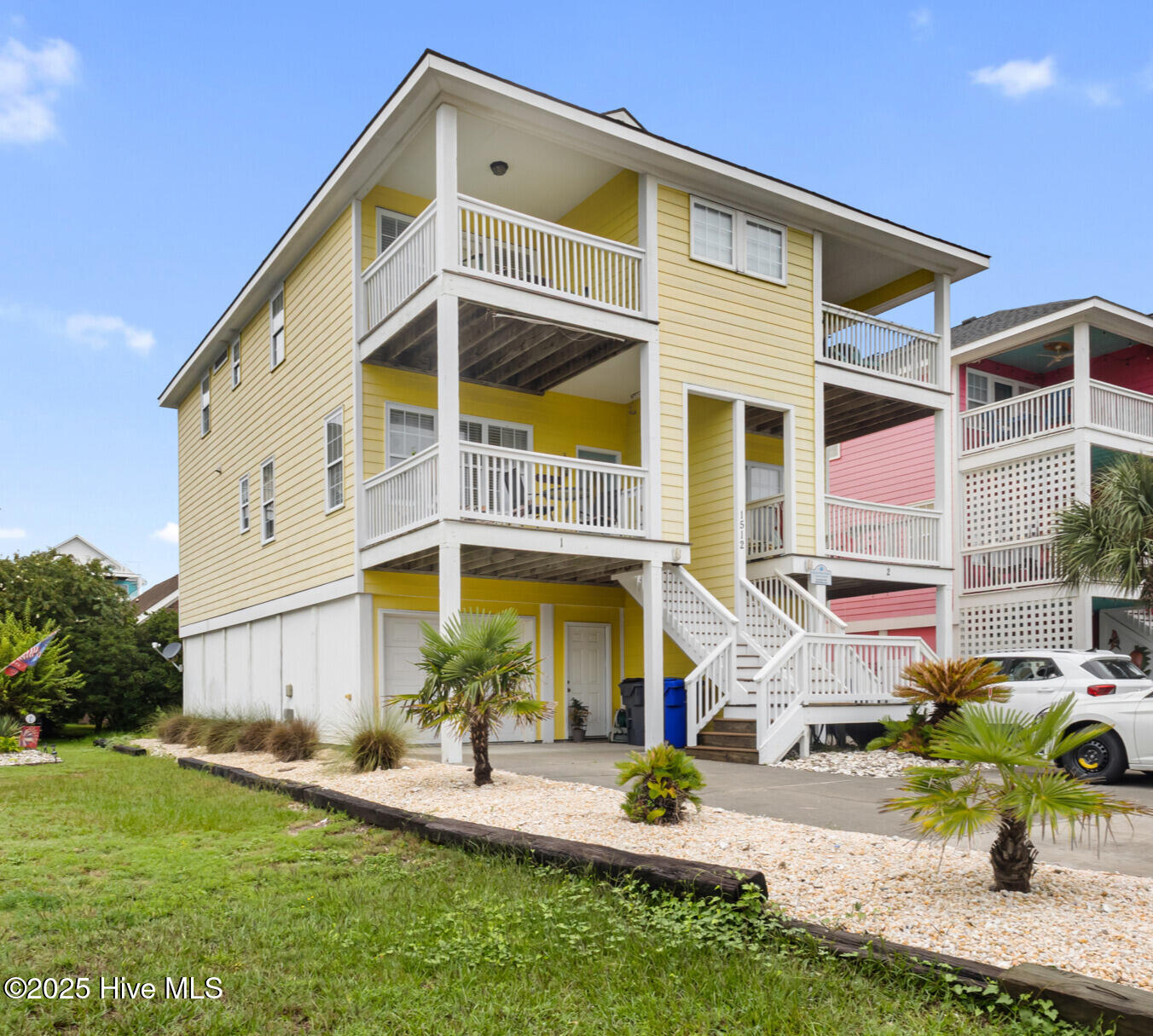 Yellow coastal home with multiple white-railed balconies, exterior stairs, and palm landscaping.