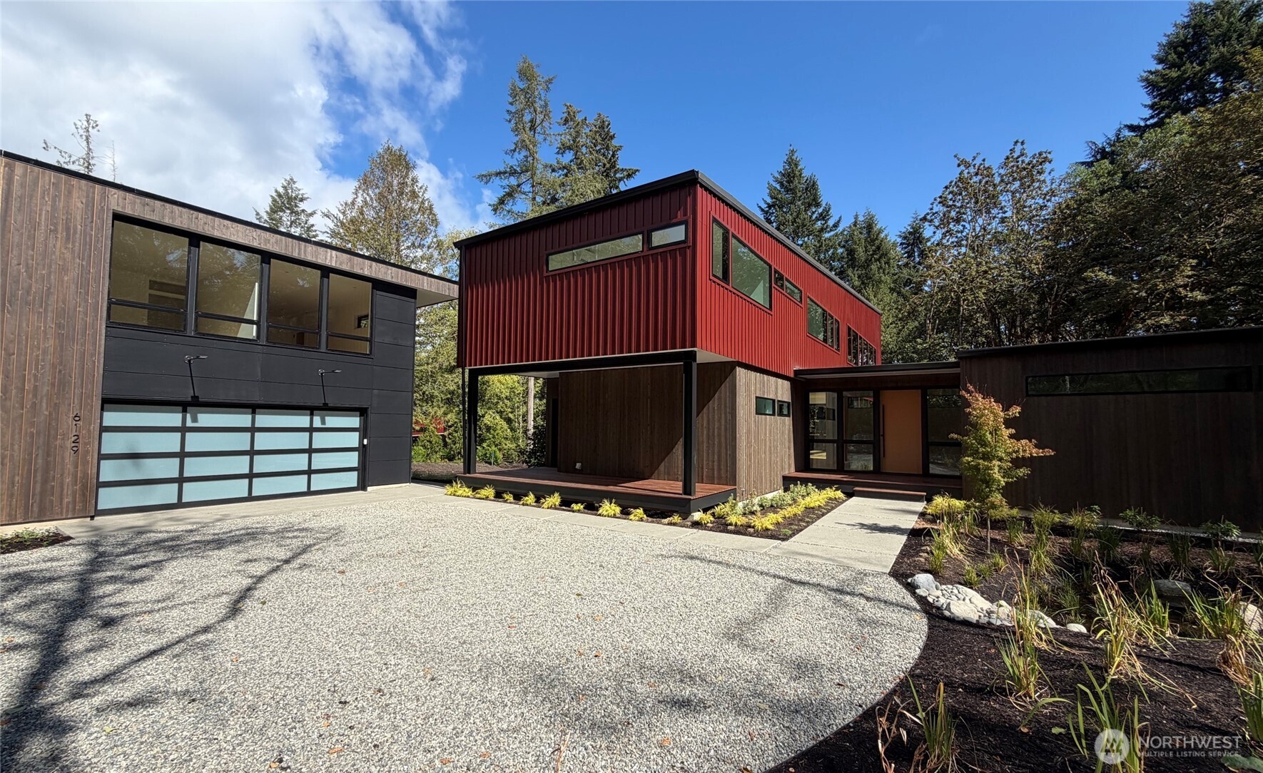 Modern home with a red upper story, dark siding, and a curved gravel driveway.