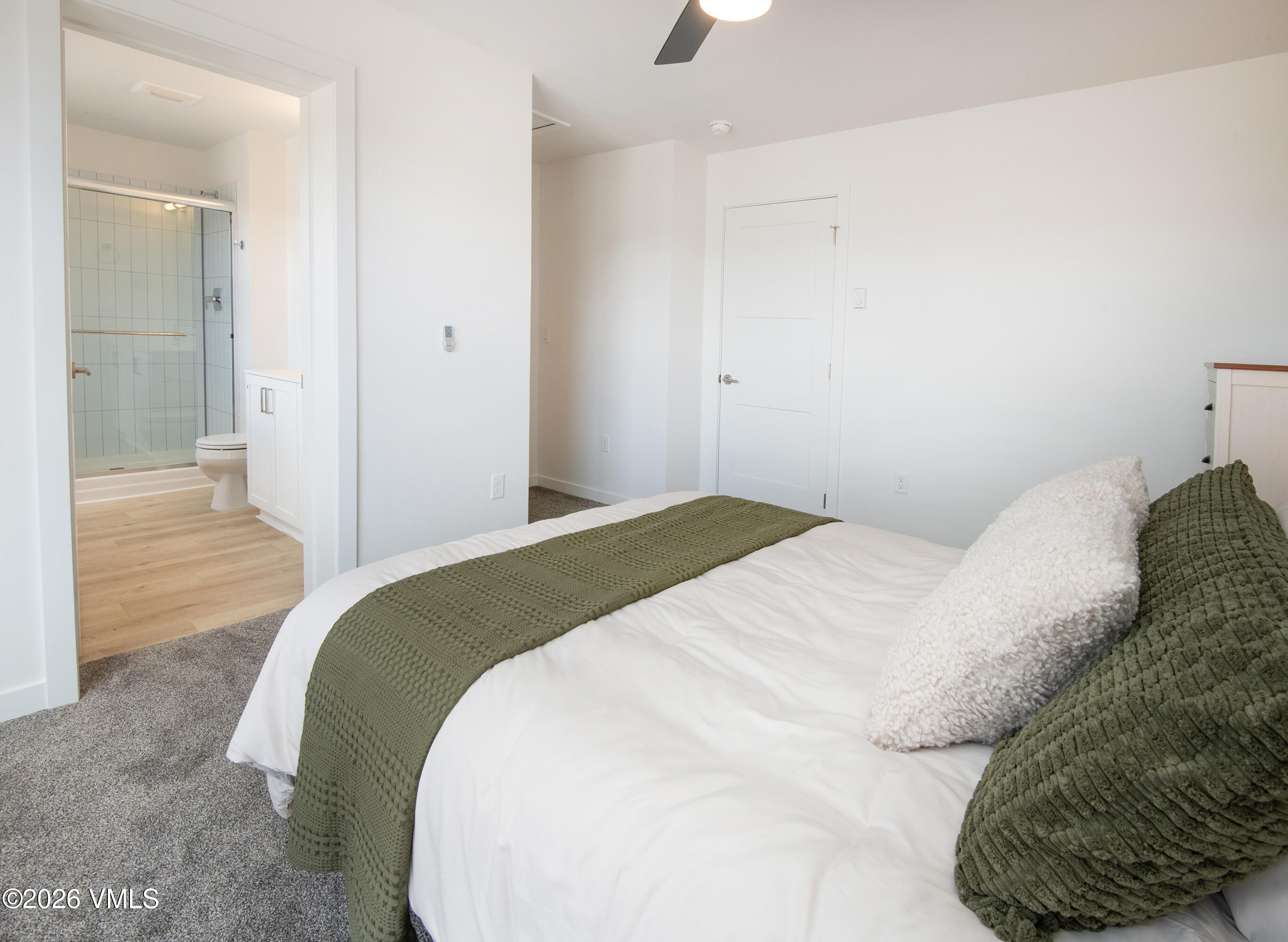 Staged bedroom with green bedding and an open doorway to an ensuite bathroom.