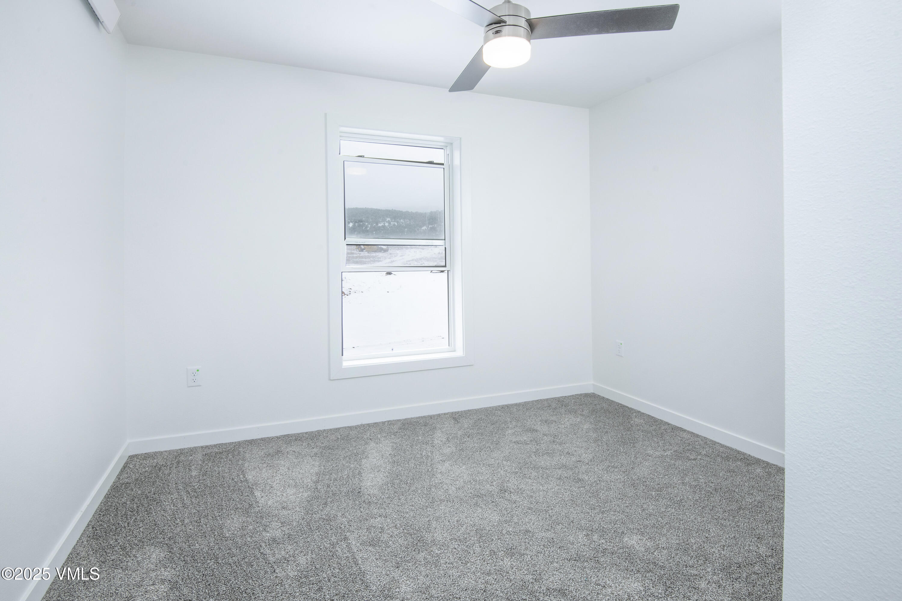 Empty carpeted room with a ceiling fan and a window overlooking snowy ground.