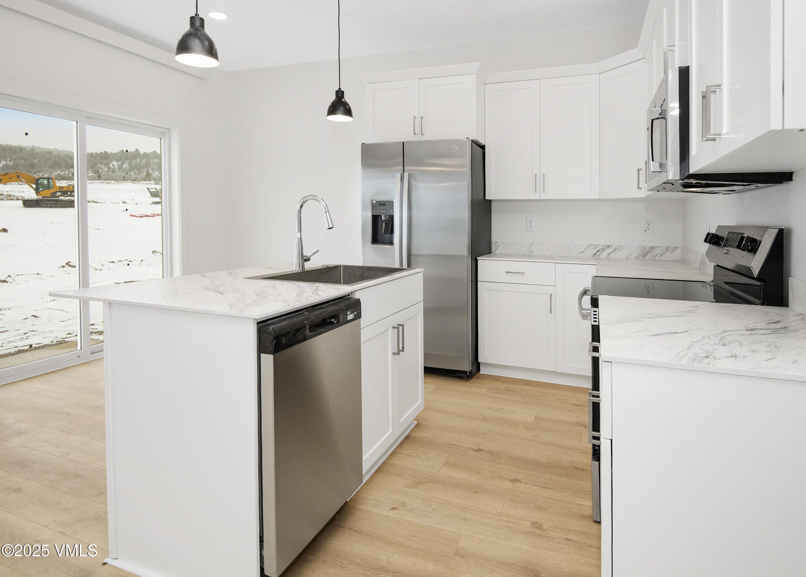 Modern white kitchen with a large island, stainless steel appliances, and snowy views through sliding glass doors.