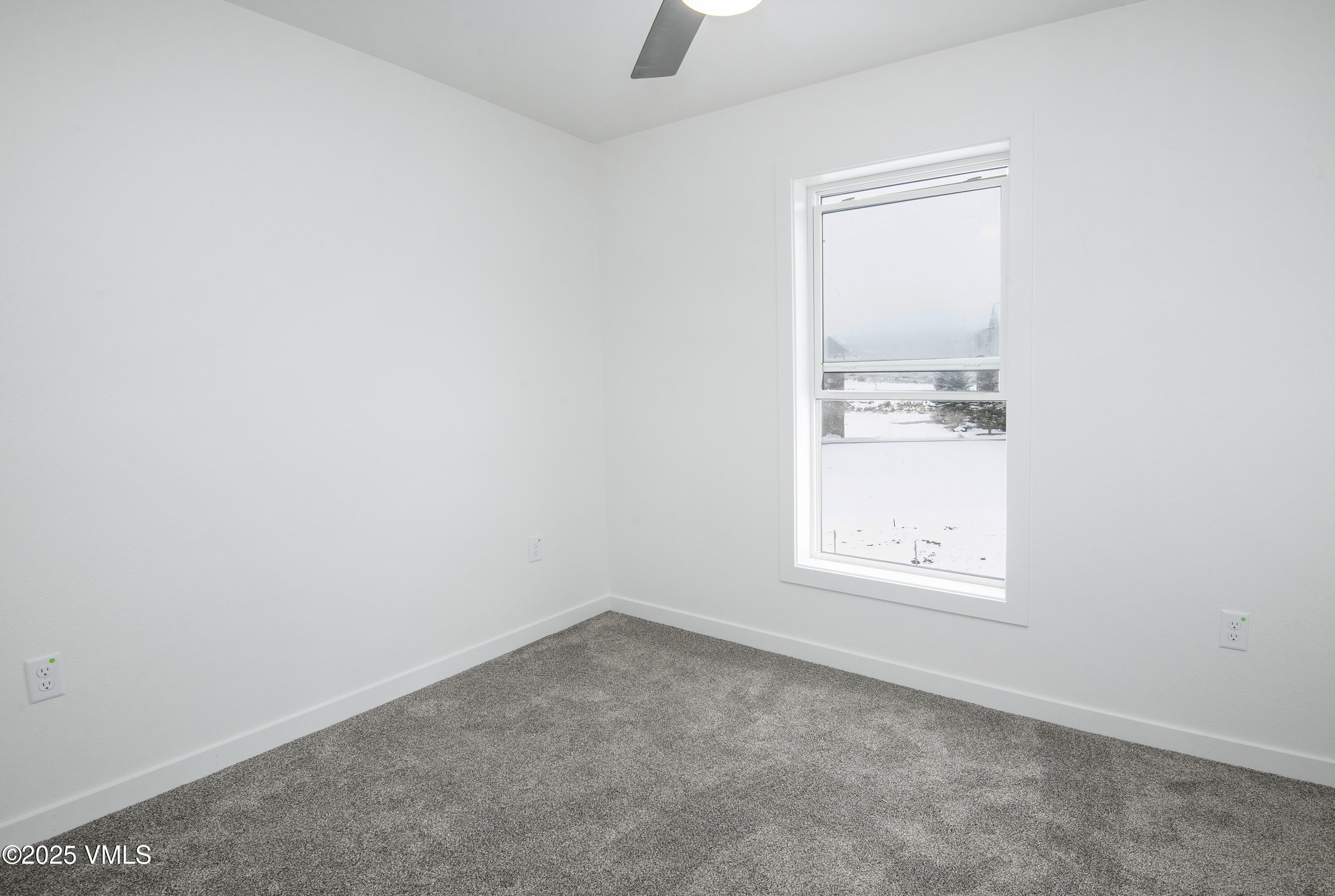 Empty carpeted room with a large window overlooking a snowy yard.