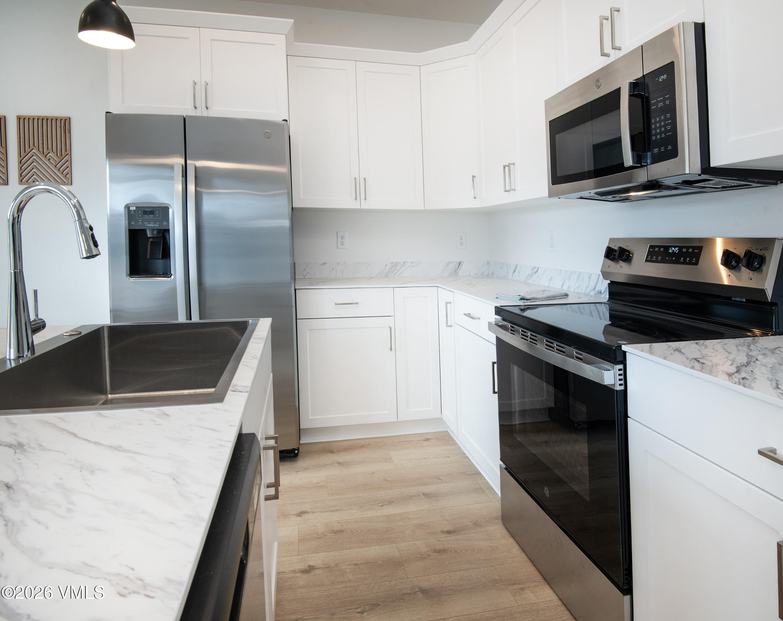 Modern kitchen with white cabinets, marble-look counters, stainless appliances, and a deep dark sink.