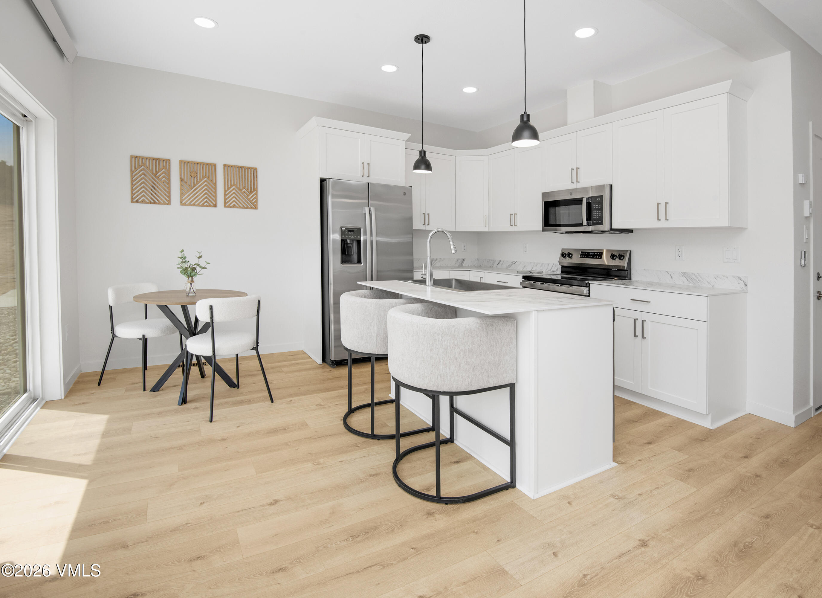 Bright white kitchen with stainless appliances, a large island, and light wood floors.