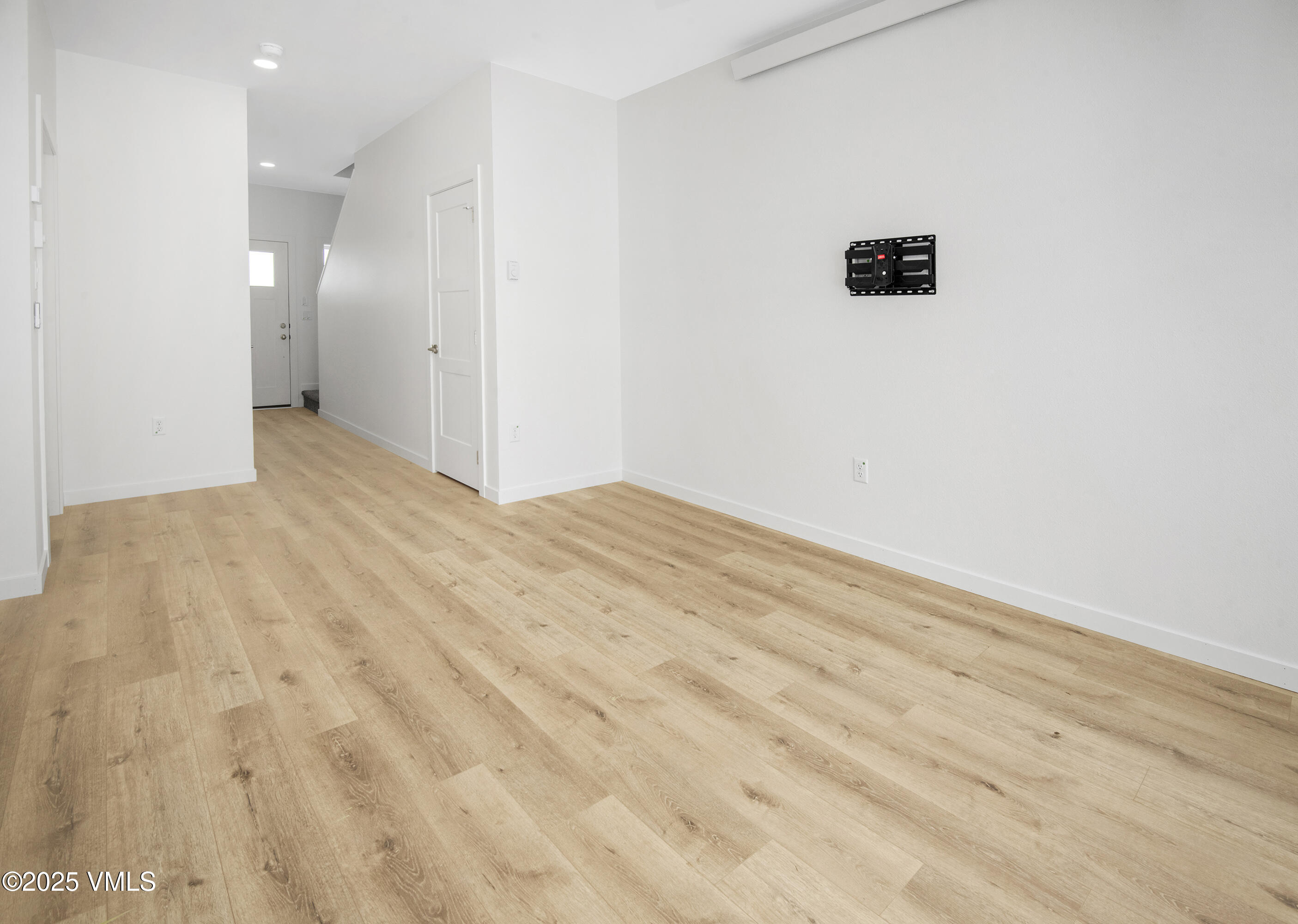 Empty room with light wood-look floors, white walls, and a wall-mounted television bracket.