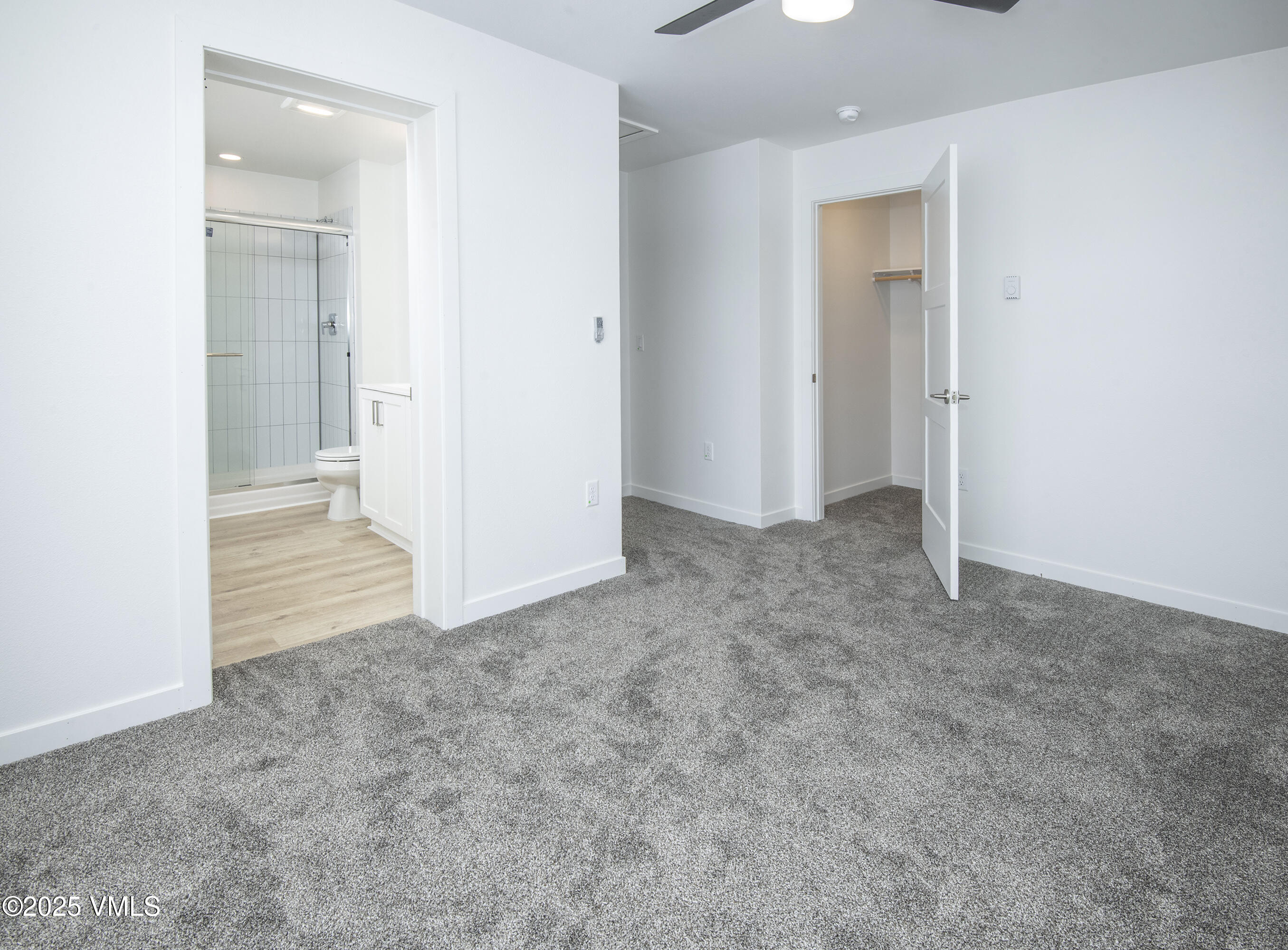 Empty carpeted bedroom with an open closet and adjoining bathroom with a tiled shower.