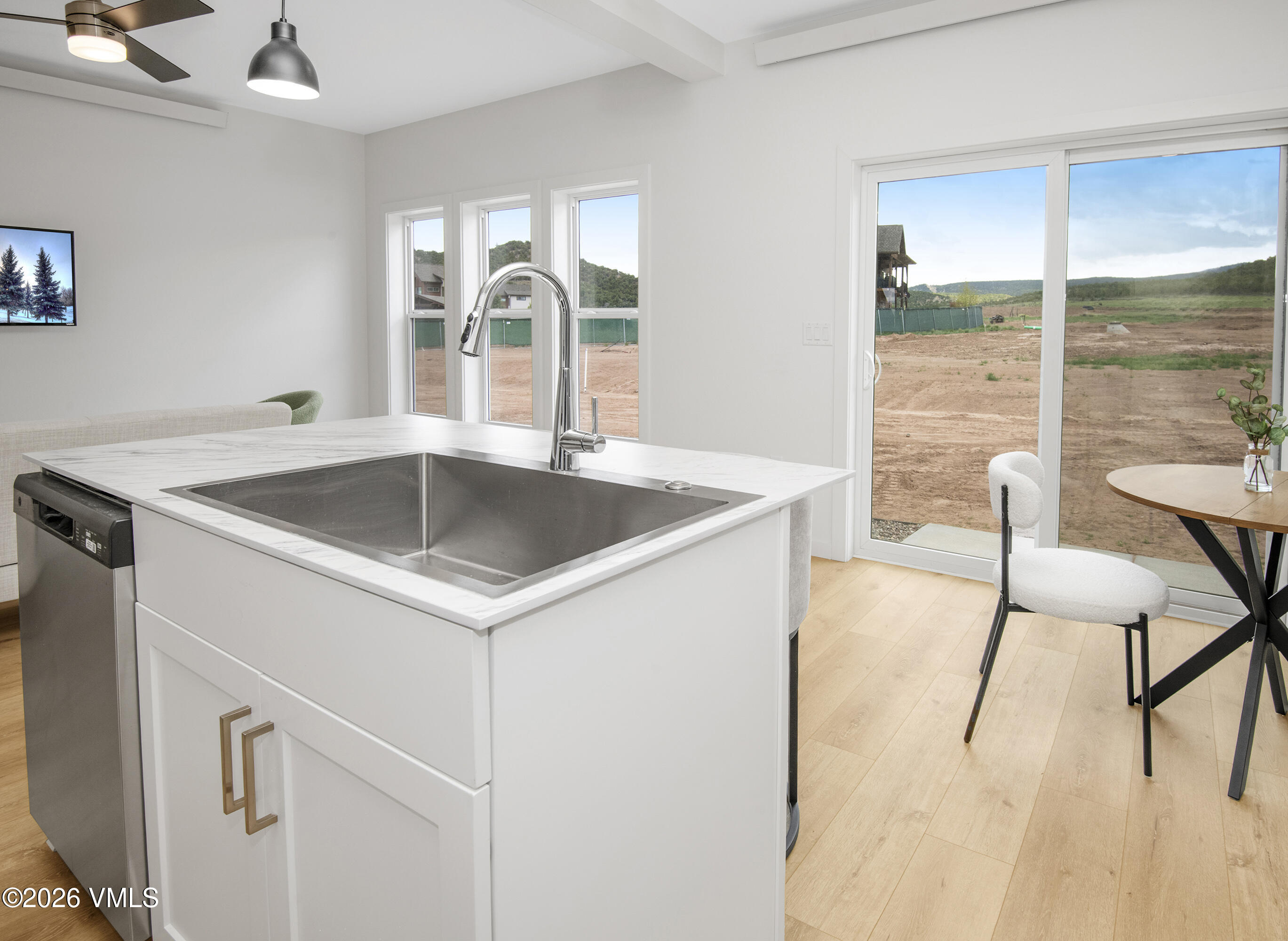 Kitchen with a large white island and stainless sink beside sliding glass doors overlooking a bare yard.