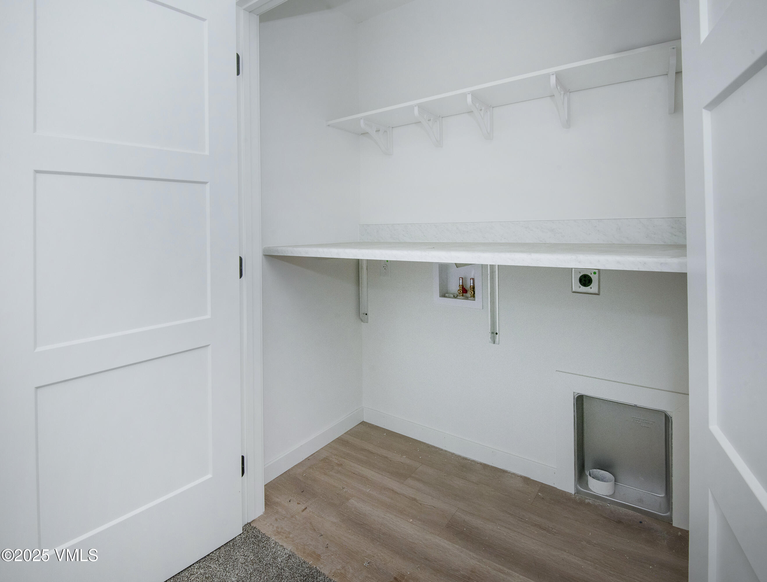 Laundry room with a long white counter, wall shelf, and plumbing connections.