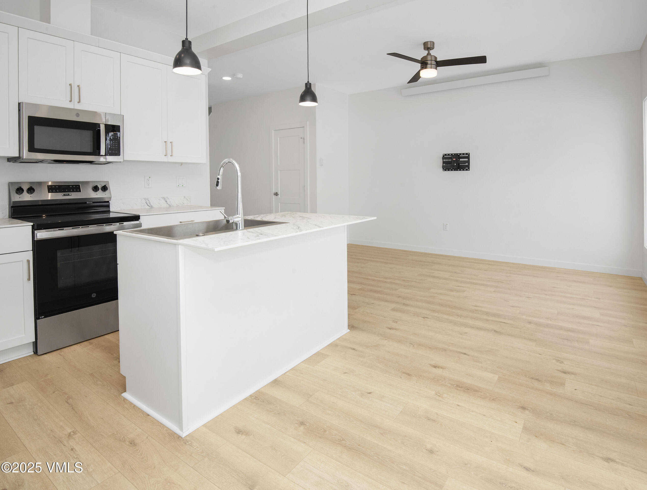 Vacant kitchen with a white island and sink, stainless steel appliances, and light wood flooring.