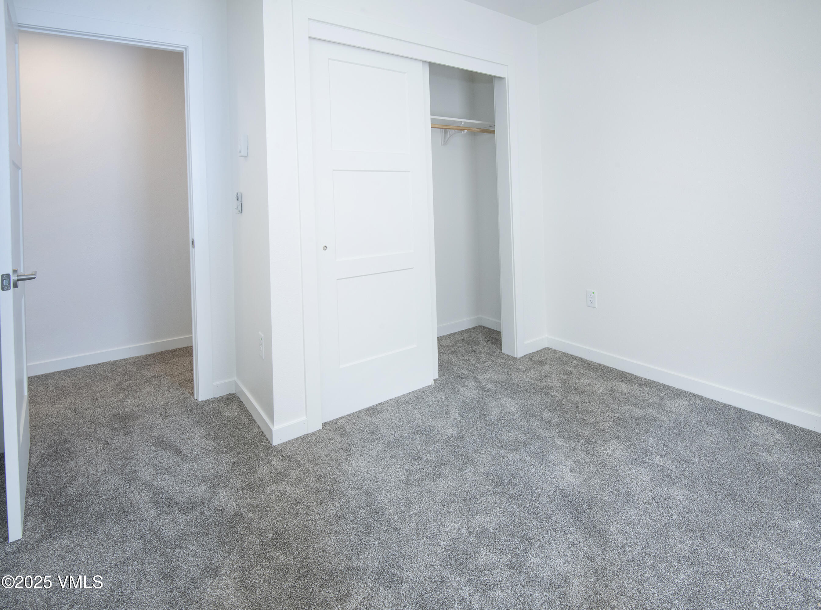 Empty bedroom with gray carpet and an open closet with a sliding door.