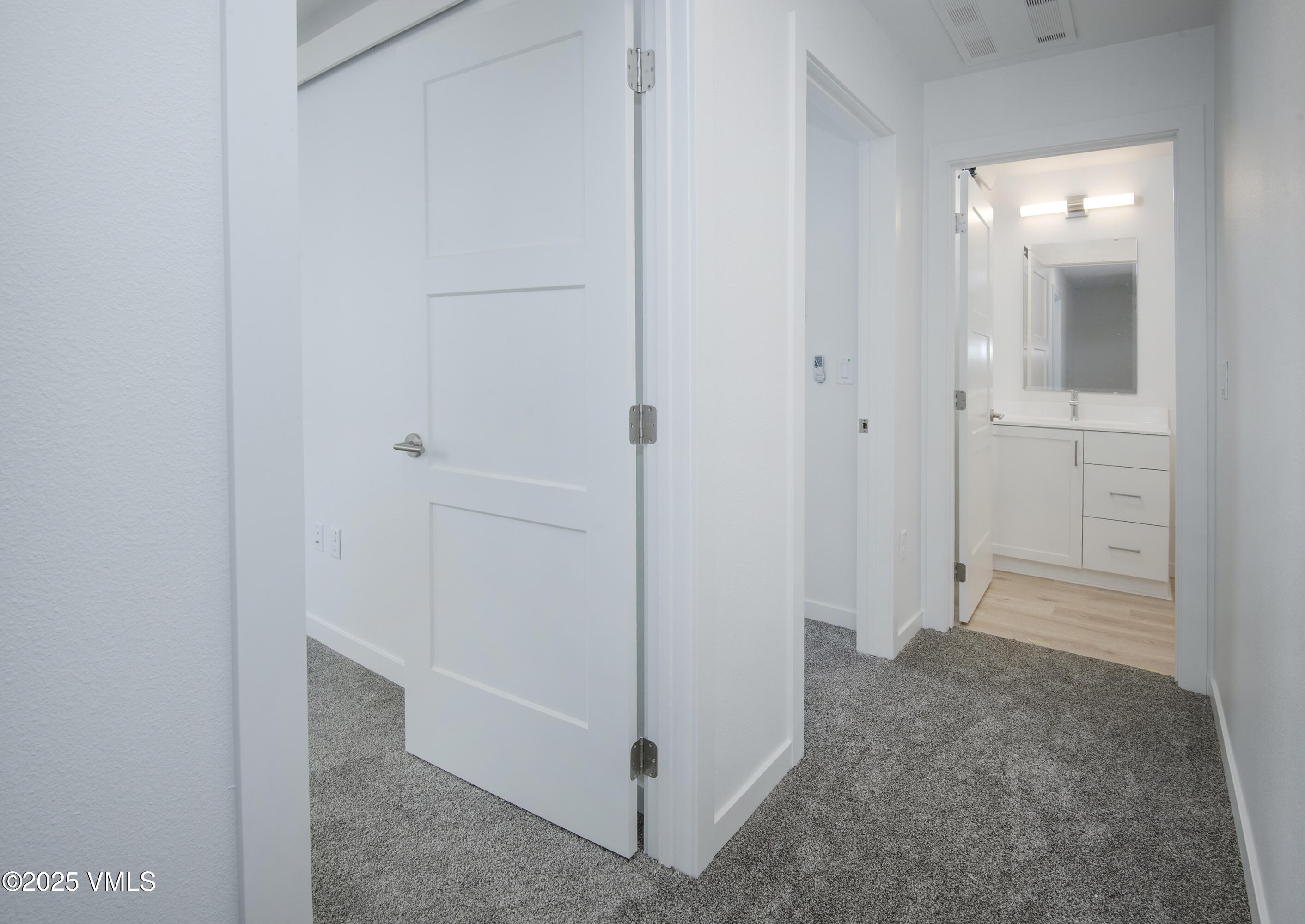 Carpeted hallway with open white doors revealing a bright bathroom and white vanity.