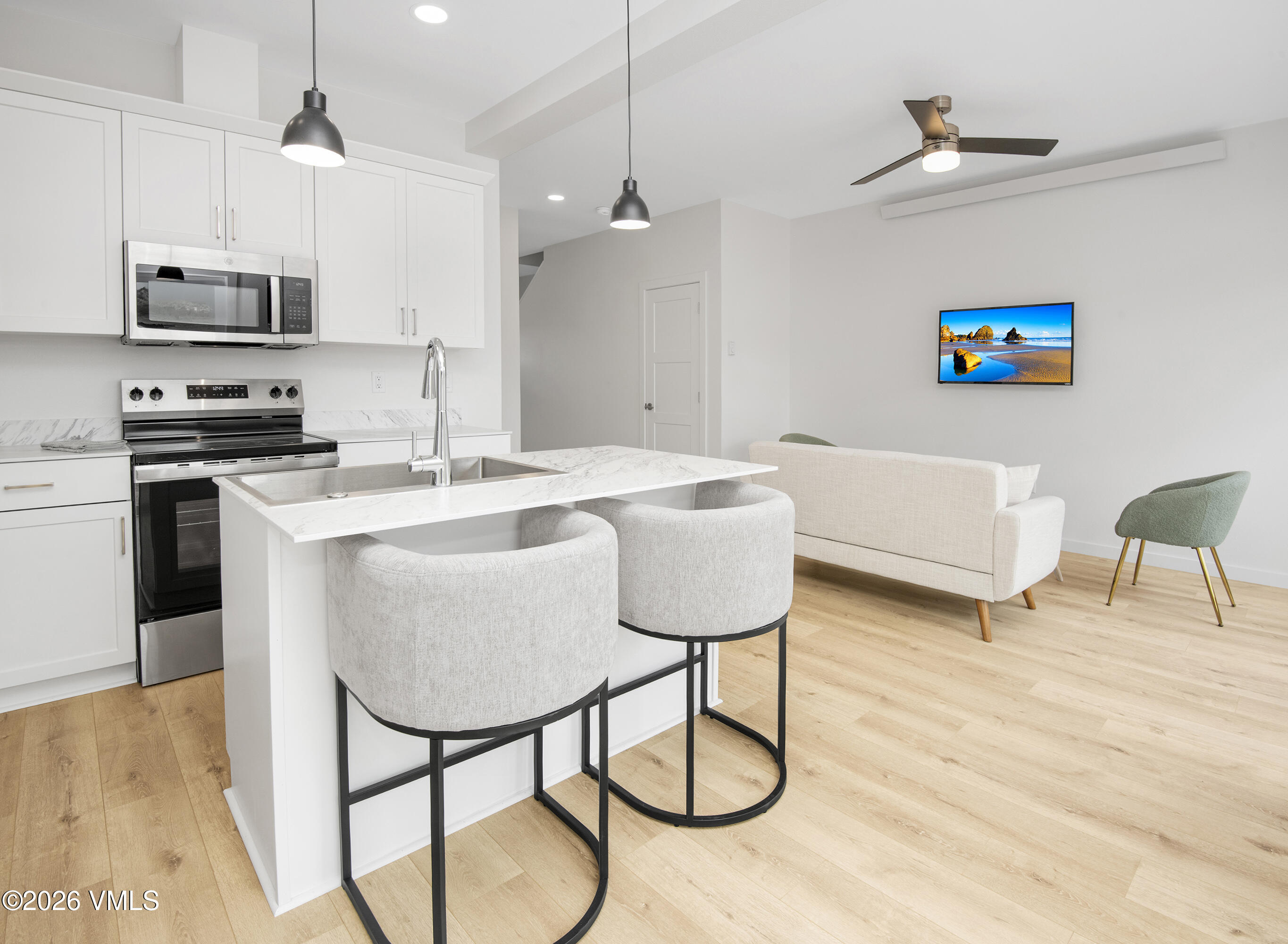 Open kitchen with white cabinetry and marble island beside a furnished living area.