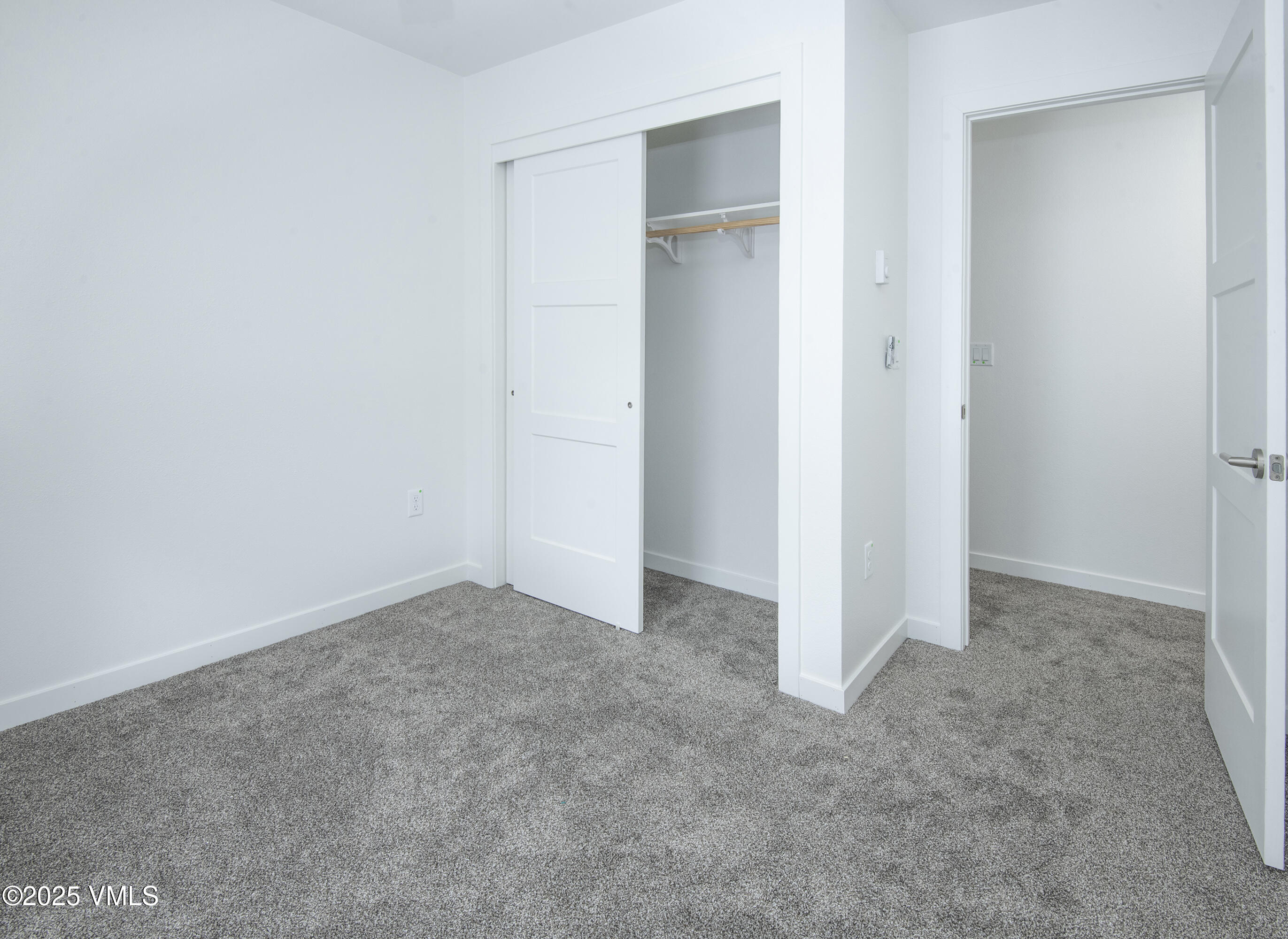 Empty carpeted bedroom with an open closet and doorway to an adjoining room.