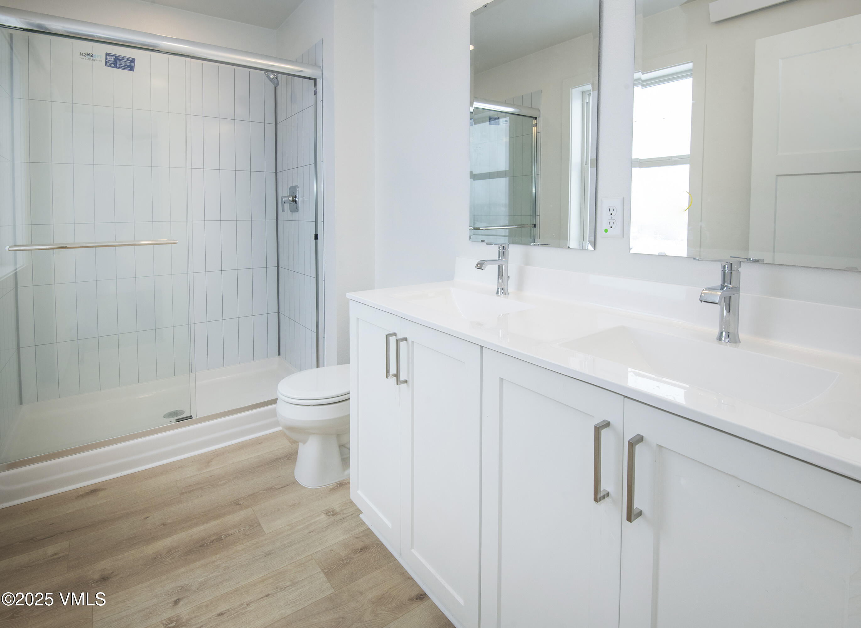 Modern bathroom with a glass shower, double vanity, and light wood-look flooring.
