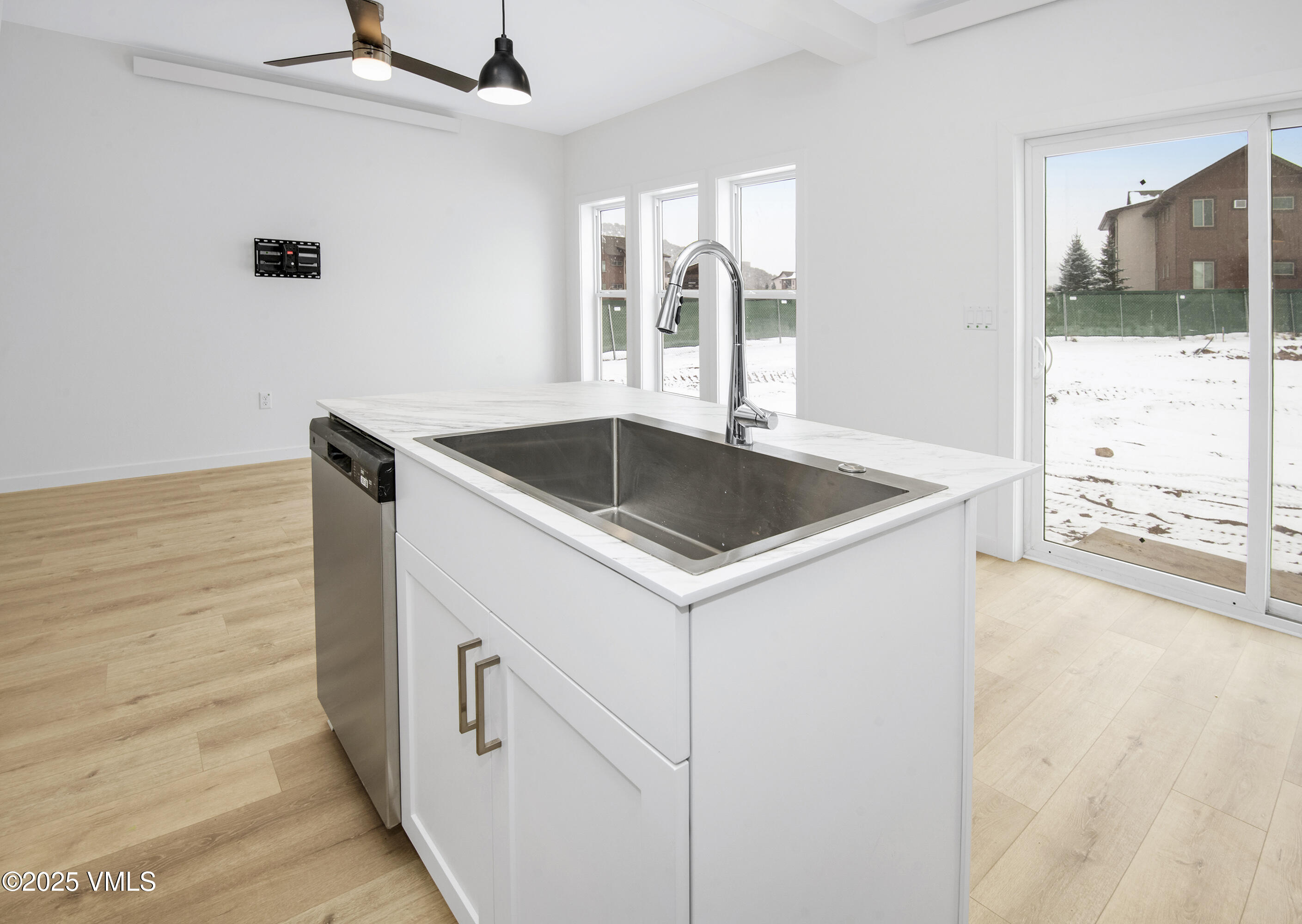 Unfurnished kitchen with a large island sink, stainless dishwasher, light wood floors, and snowy yard outside.