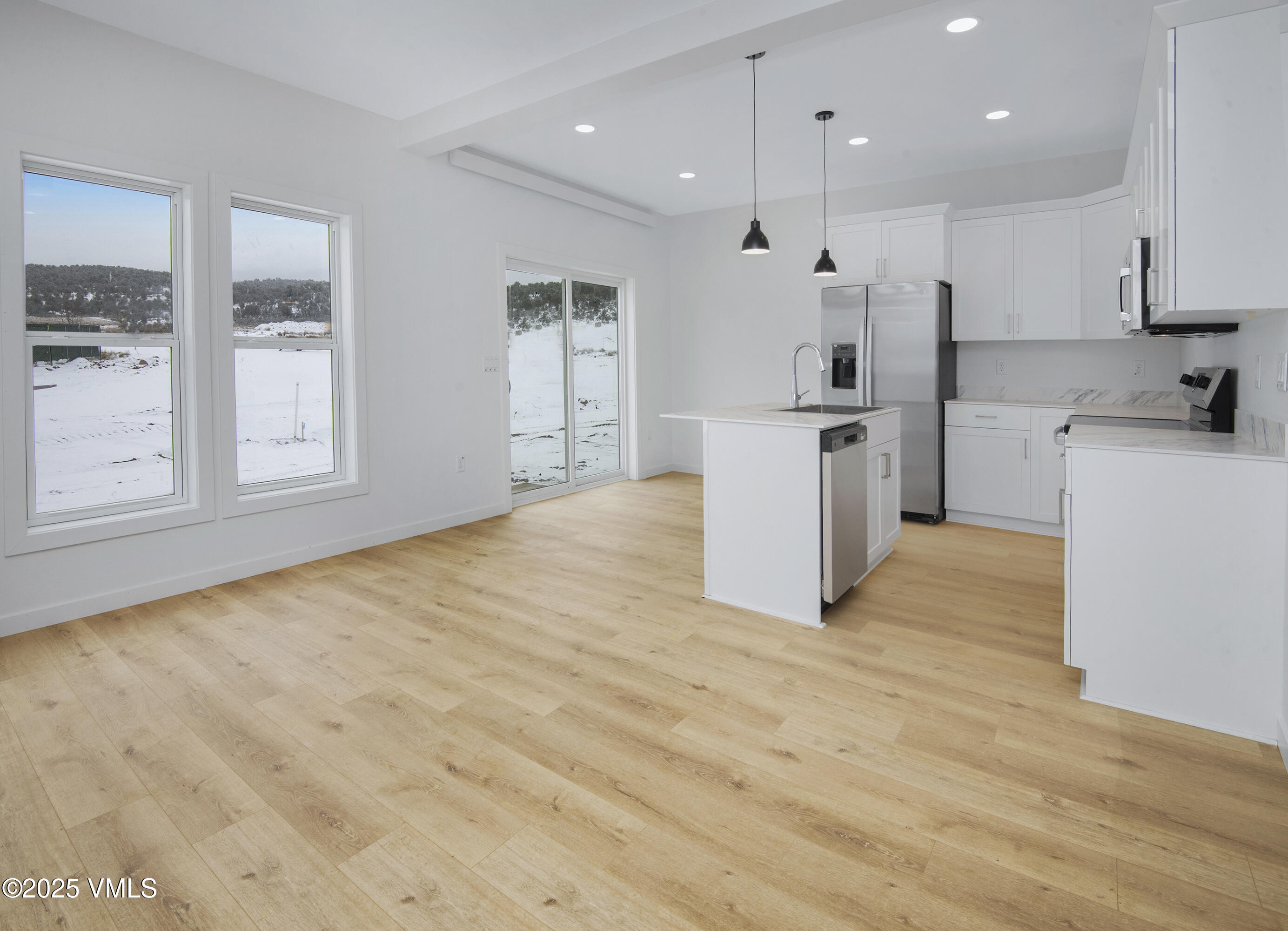 Vacant white kitchen with stainless appliances, central island, and windows overlooking snow.