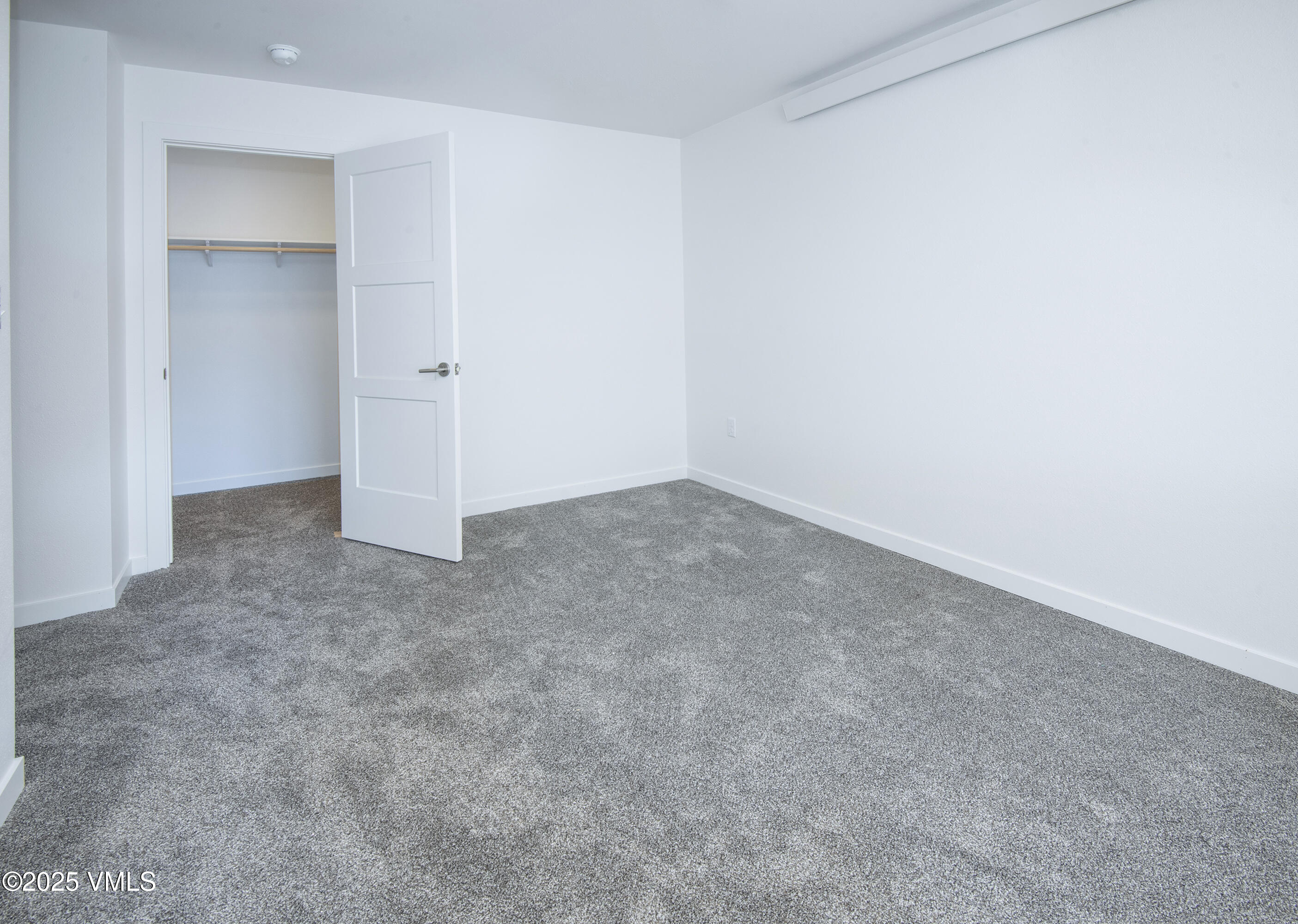 Empty bedroom with gray carpet and an open closet.