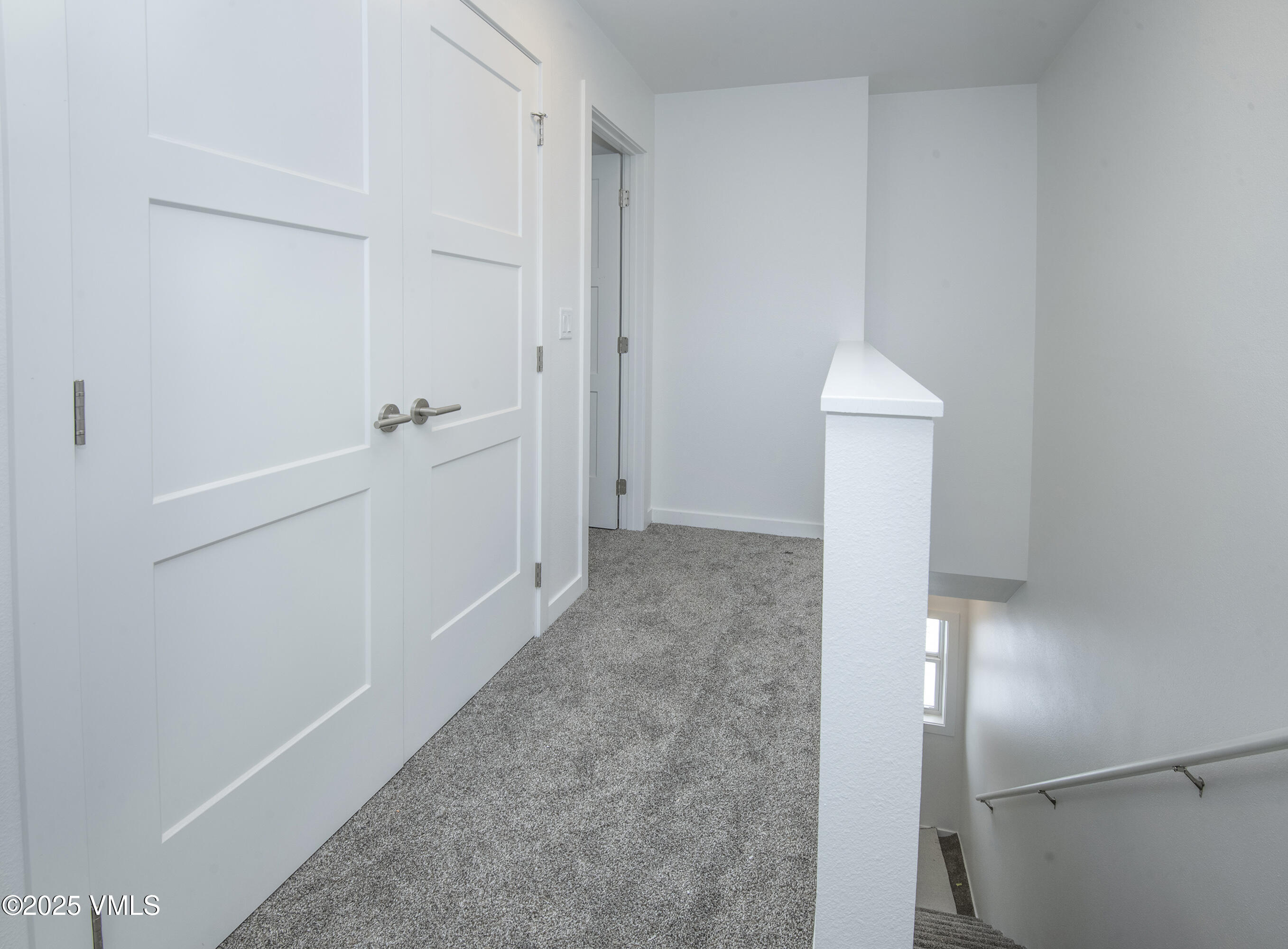 Carpeted upstairs landing with white paneled doors and stairs descending beside a window.