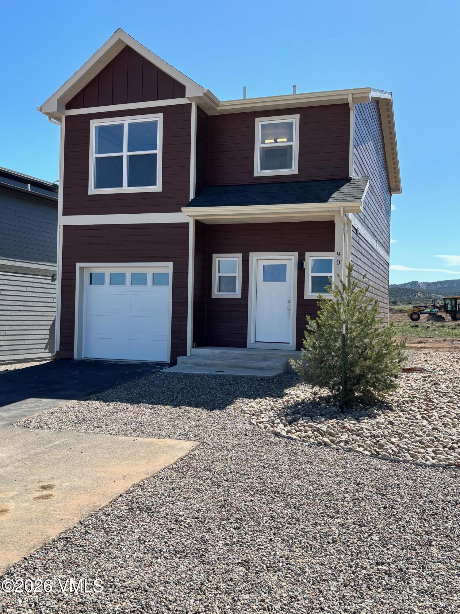 Two-story brown house with white trim, a single-car garage, and a gravel yard.