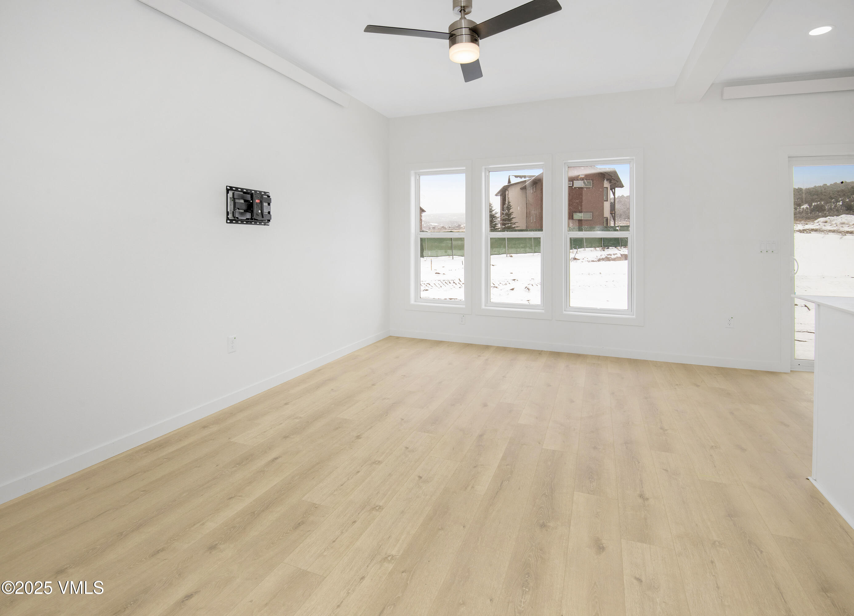 Empty room with light wood floors, a ceiling fan, and tall windows overlooking snow.
