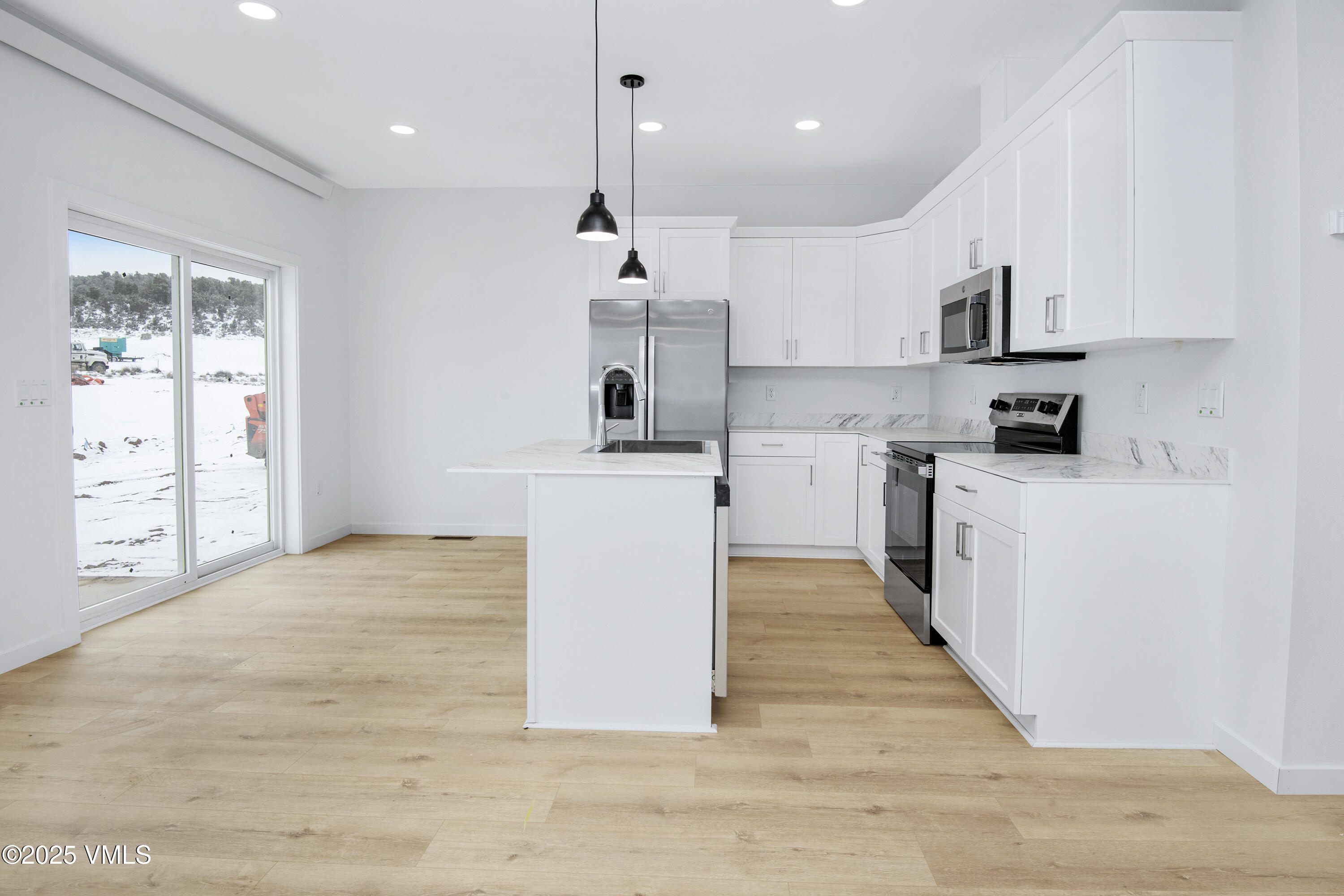 Modern white kitchen with a central island, stainless steel appliances, and sliding doors overlooking snow.