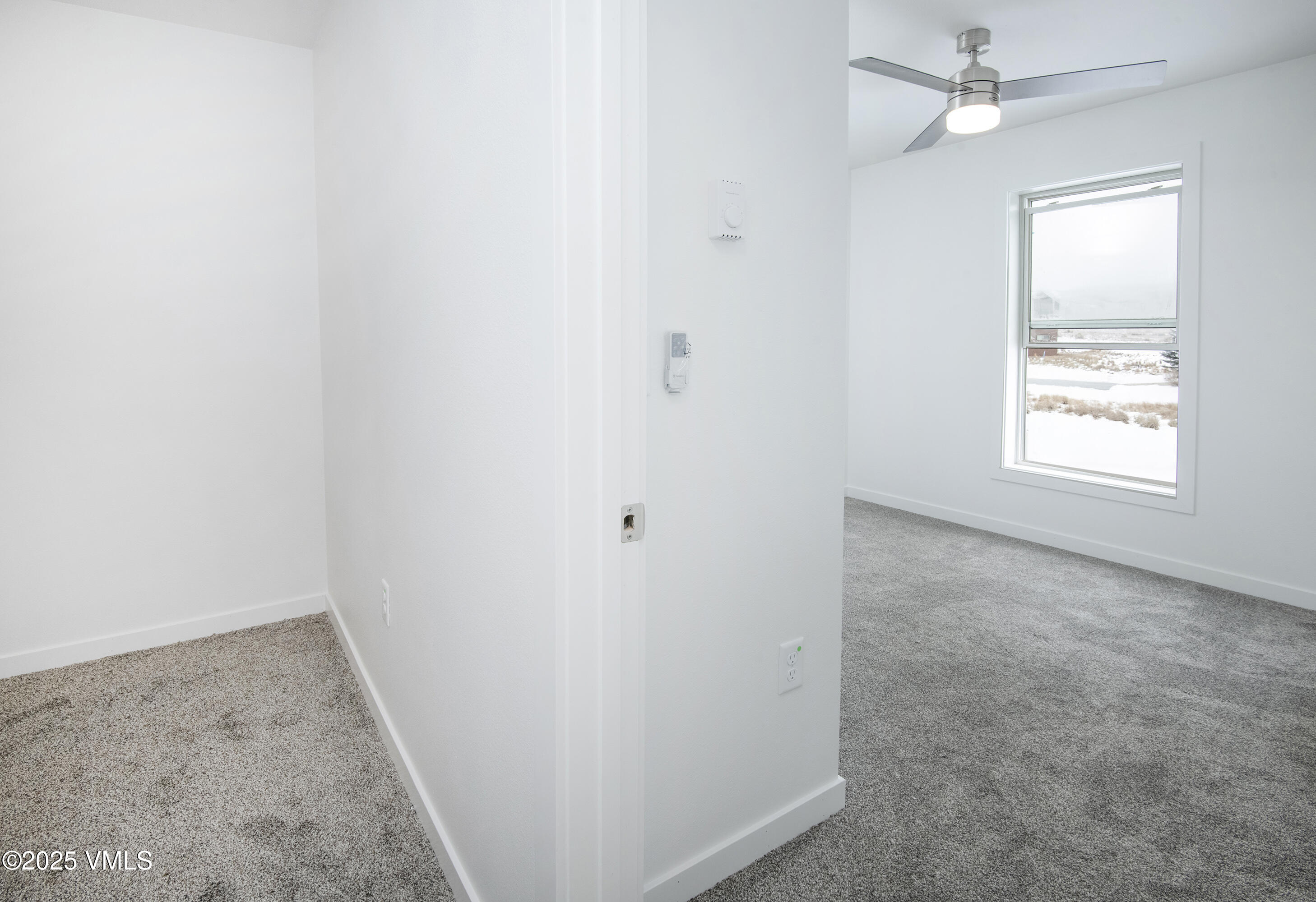 Empty carpeted bedroom with a ceiling fan and a window overlooking snow.