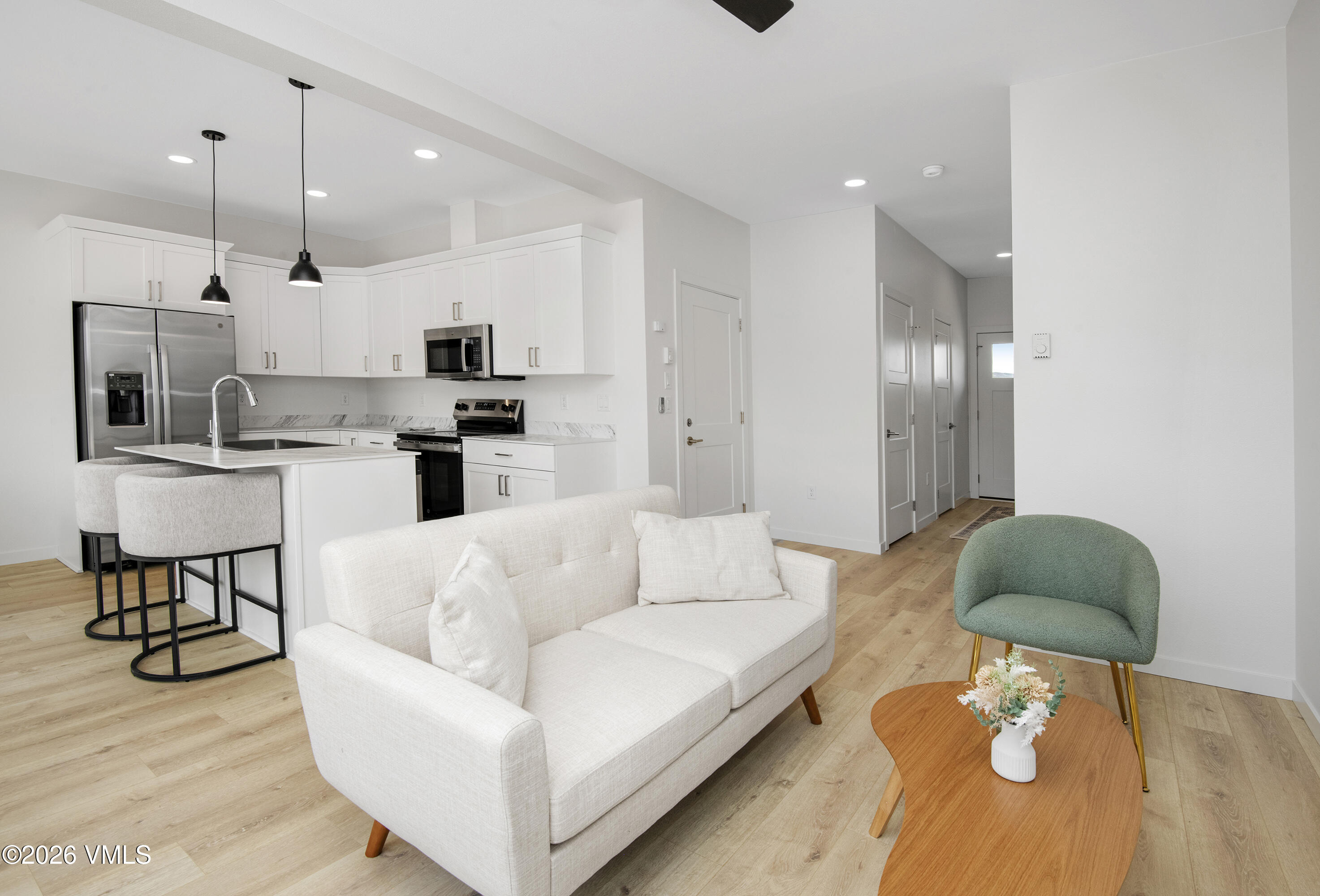 Open-plan living room and kitchen with a white sofa, green accent chair, and stainless steel appliances.