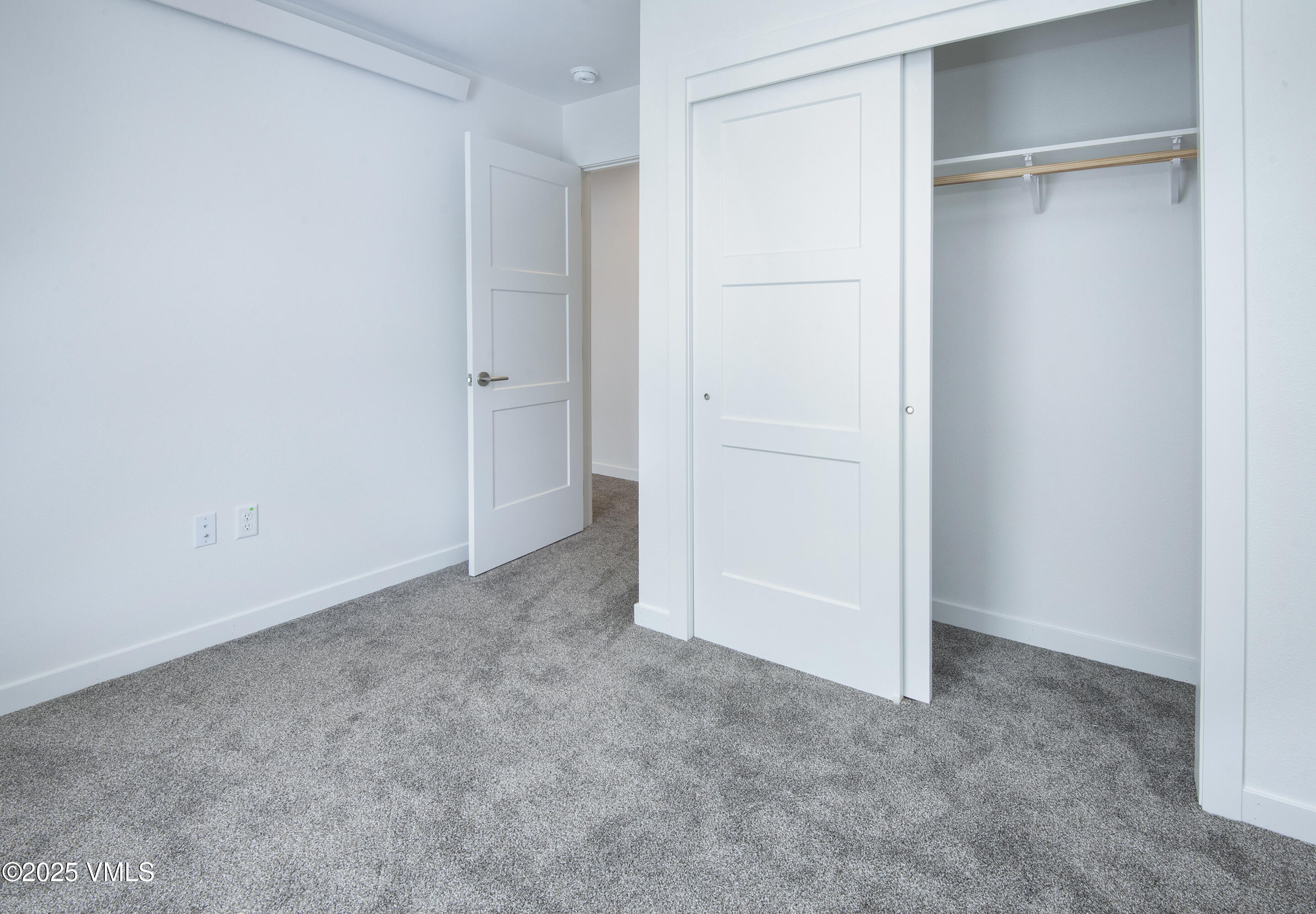 Empty bedroom with gray carpet and a large closet with a hanging rod and shelf.