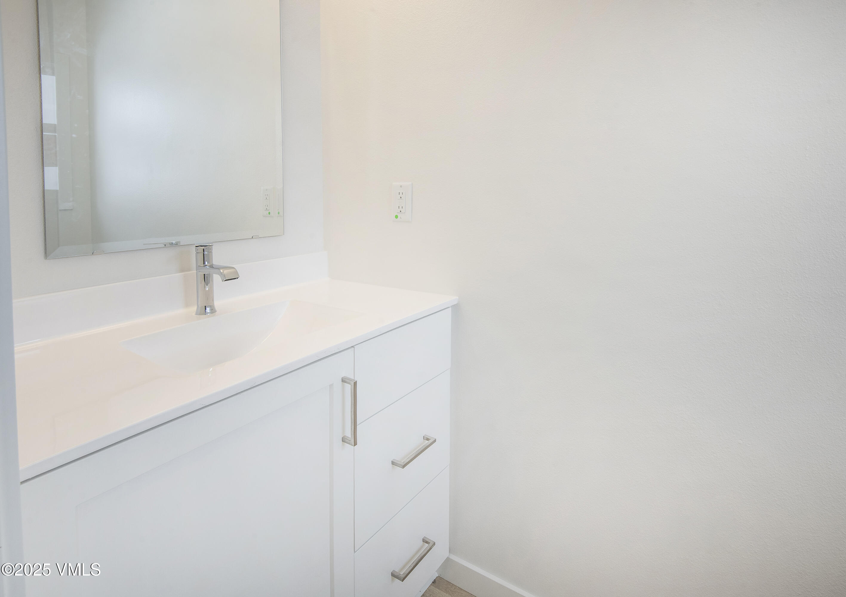 Bathroom vanity with integrated white sink, chrome faucet, large mirror, and white drawers.