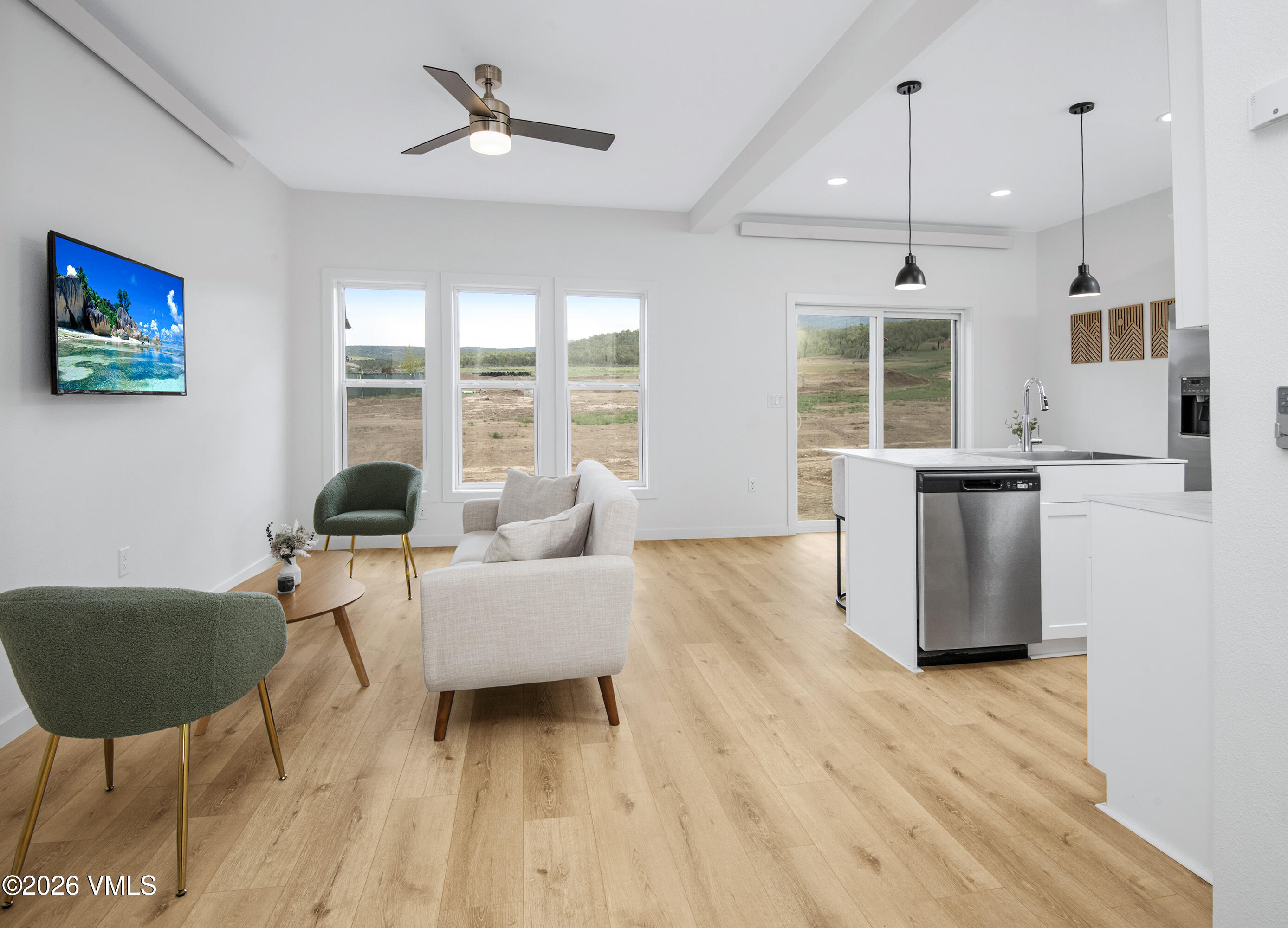 Open-plan living room and kitchen with pale wood floors, large windows, and a white island.