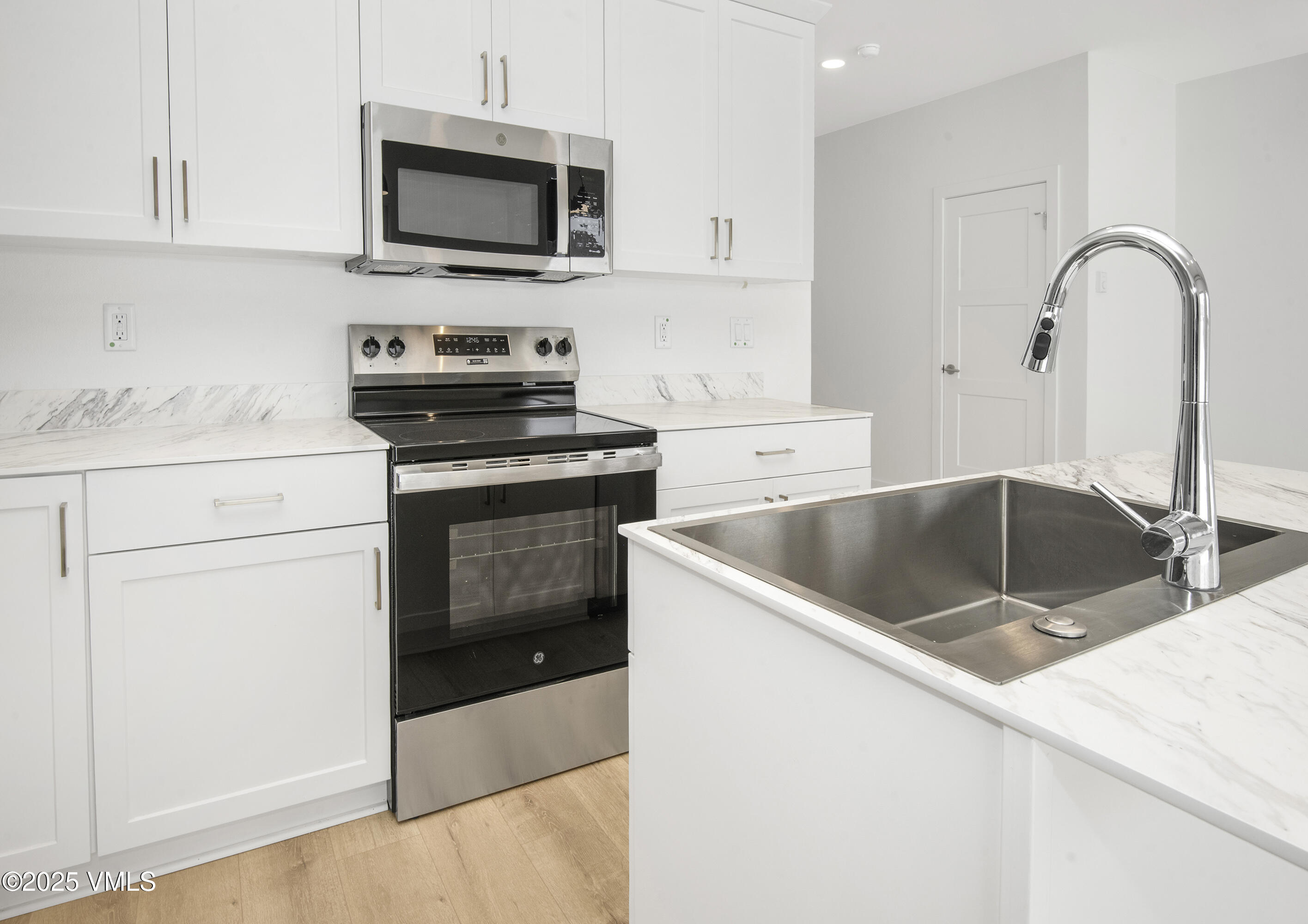 Kitchen with white shaker cabinets, stainless steel appliances, marble-look counters, and a large undermount sink.