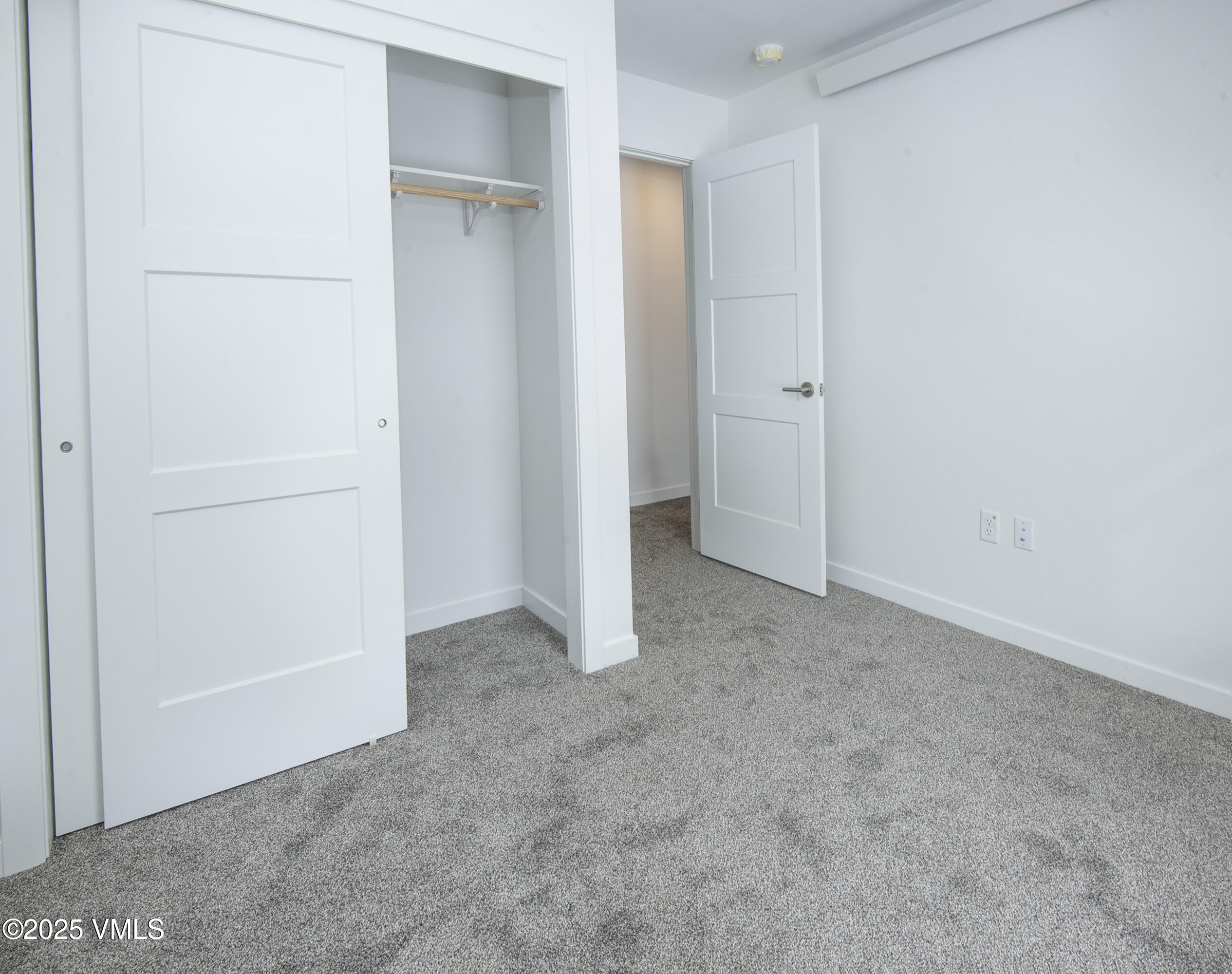 Empty carpeted bedroom with an open closet and white paneled doors.