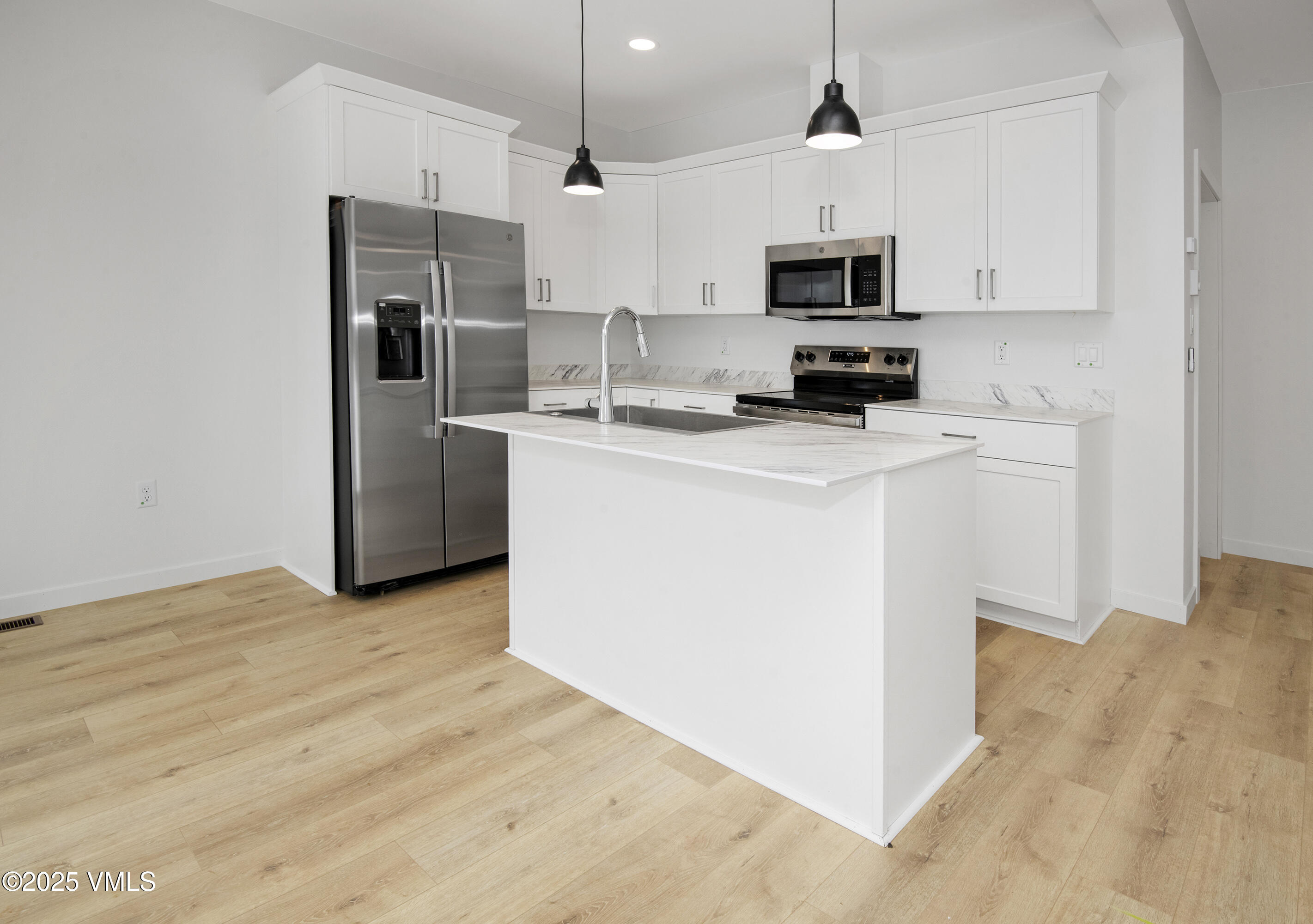 Modern kitchen with a large sink island, white cabinets, stainless steel appliances, and light wood floors.