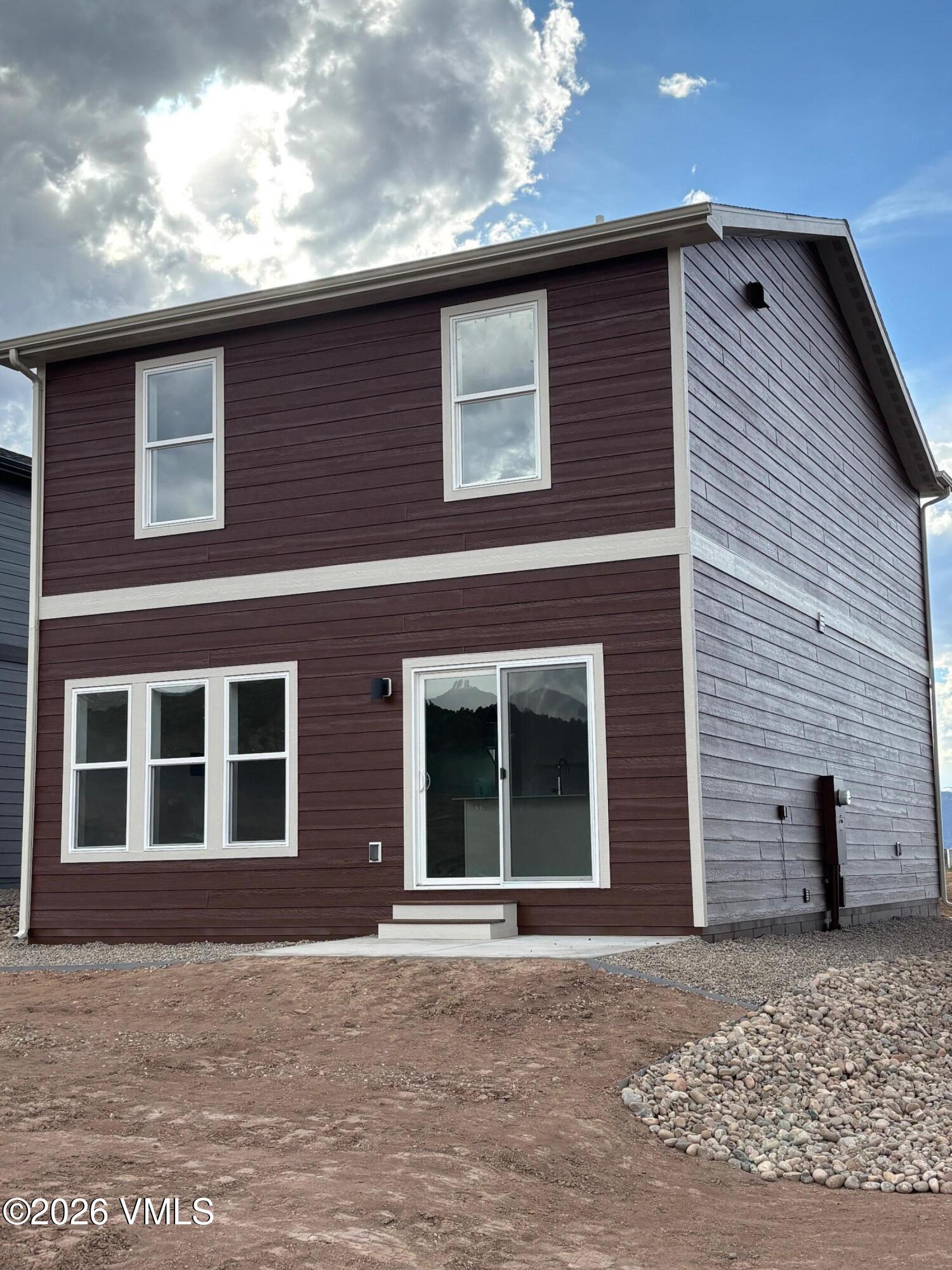 Two-story house with dark siding, white-trimmed windows, and unfinished dirt and rock landscaping.