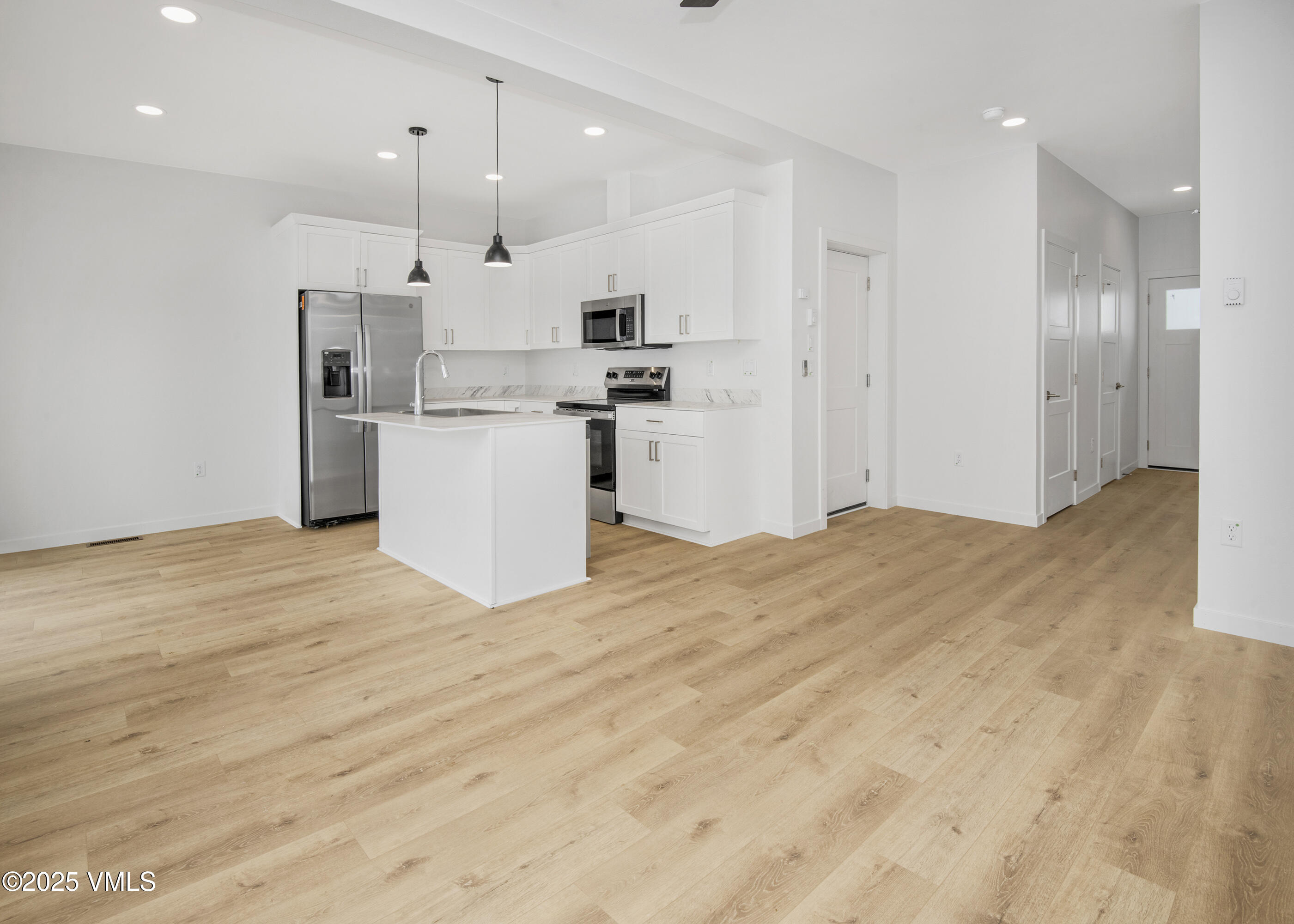 Open kitchen with white cabinets, stainless steel appliances, a center island, and light wood floors.
