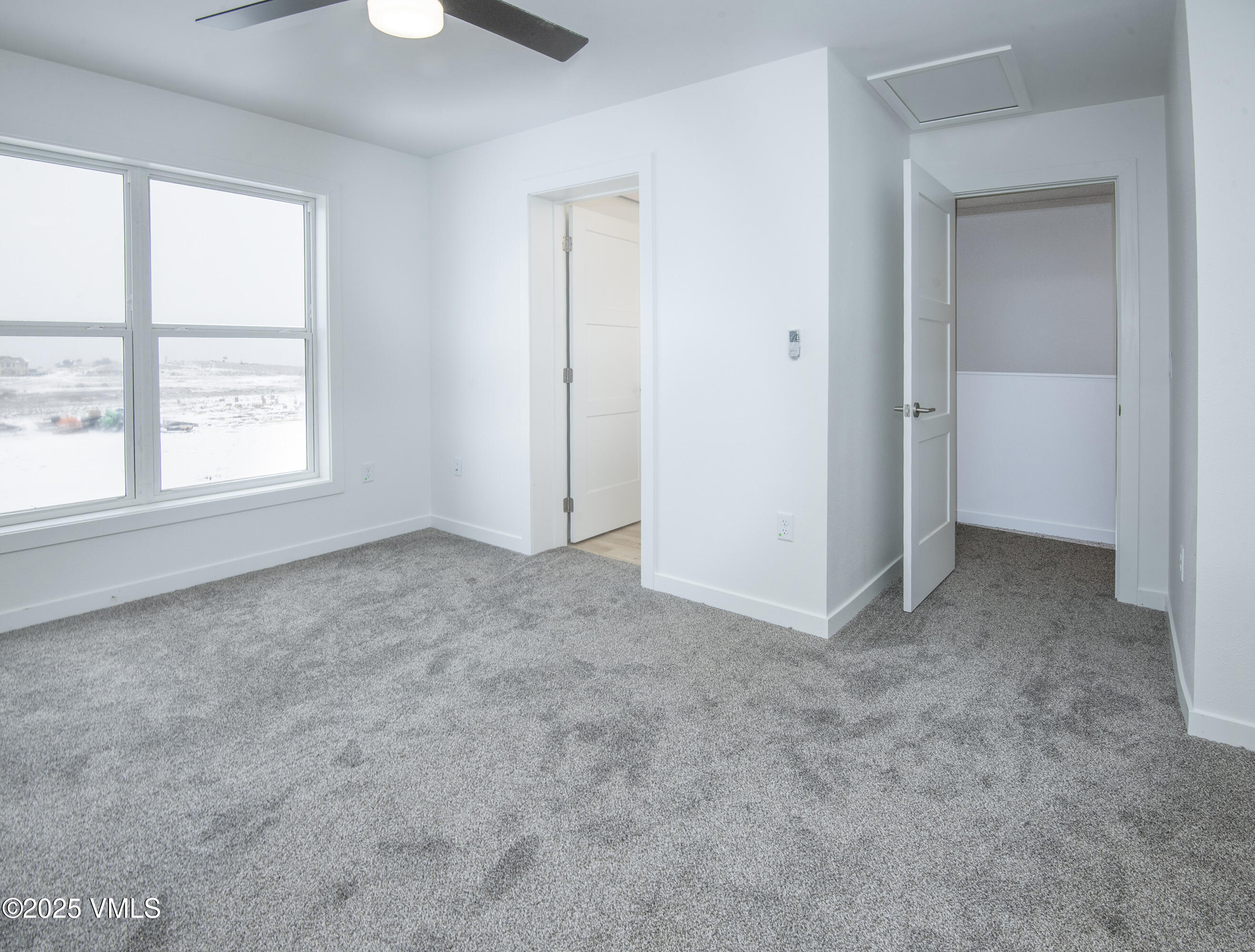 Vacant carpeted bedroom with large windows overlooking a snowy landscape and two open doorways.