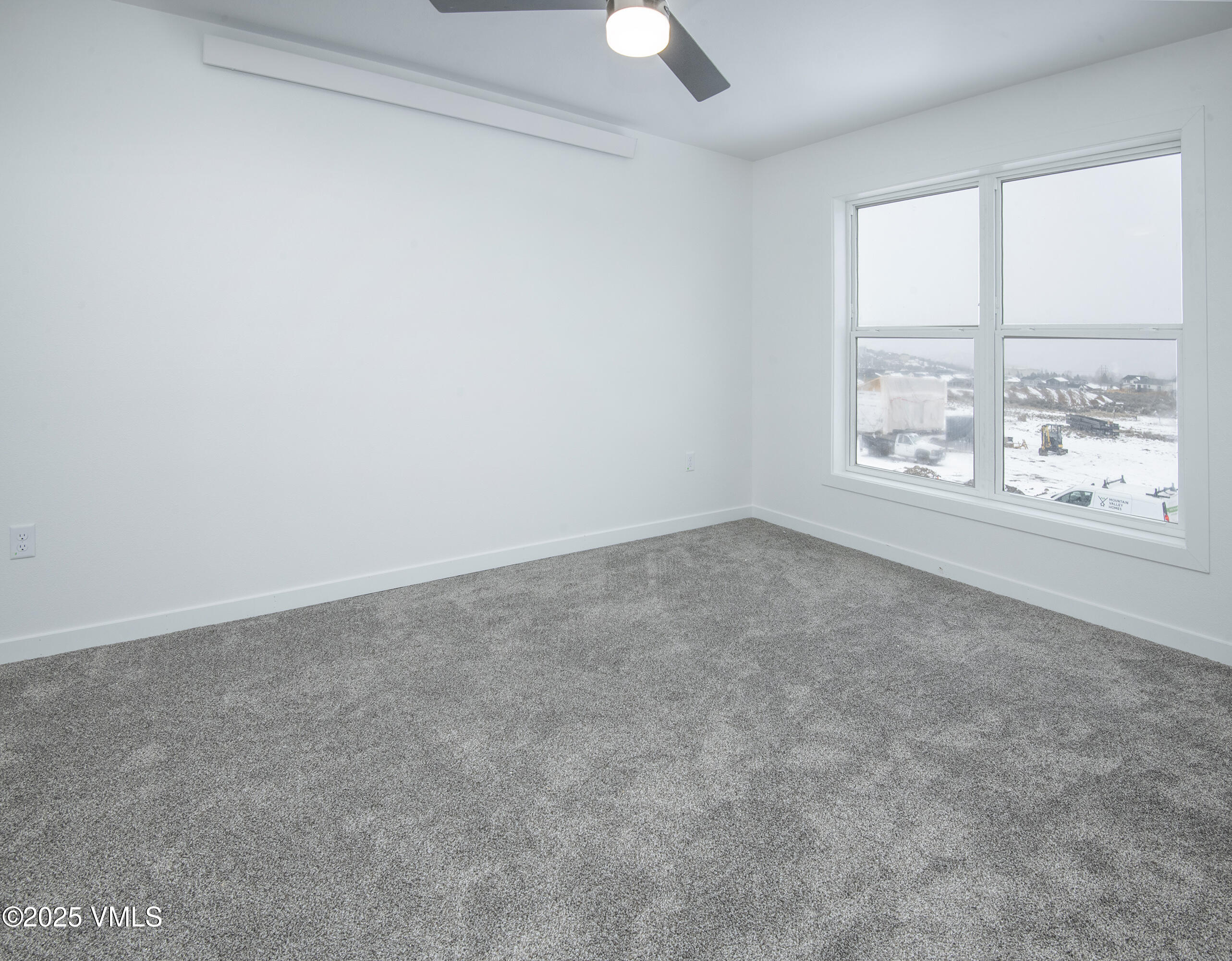 Empty bedroom with gray carpet and a large window overlooking a snowy construction site.