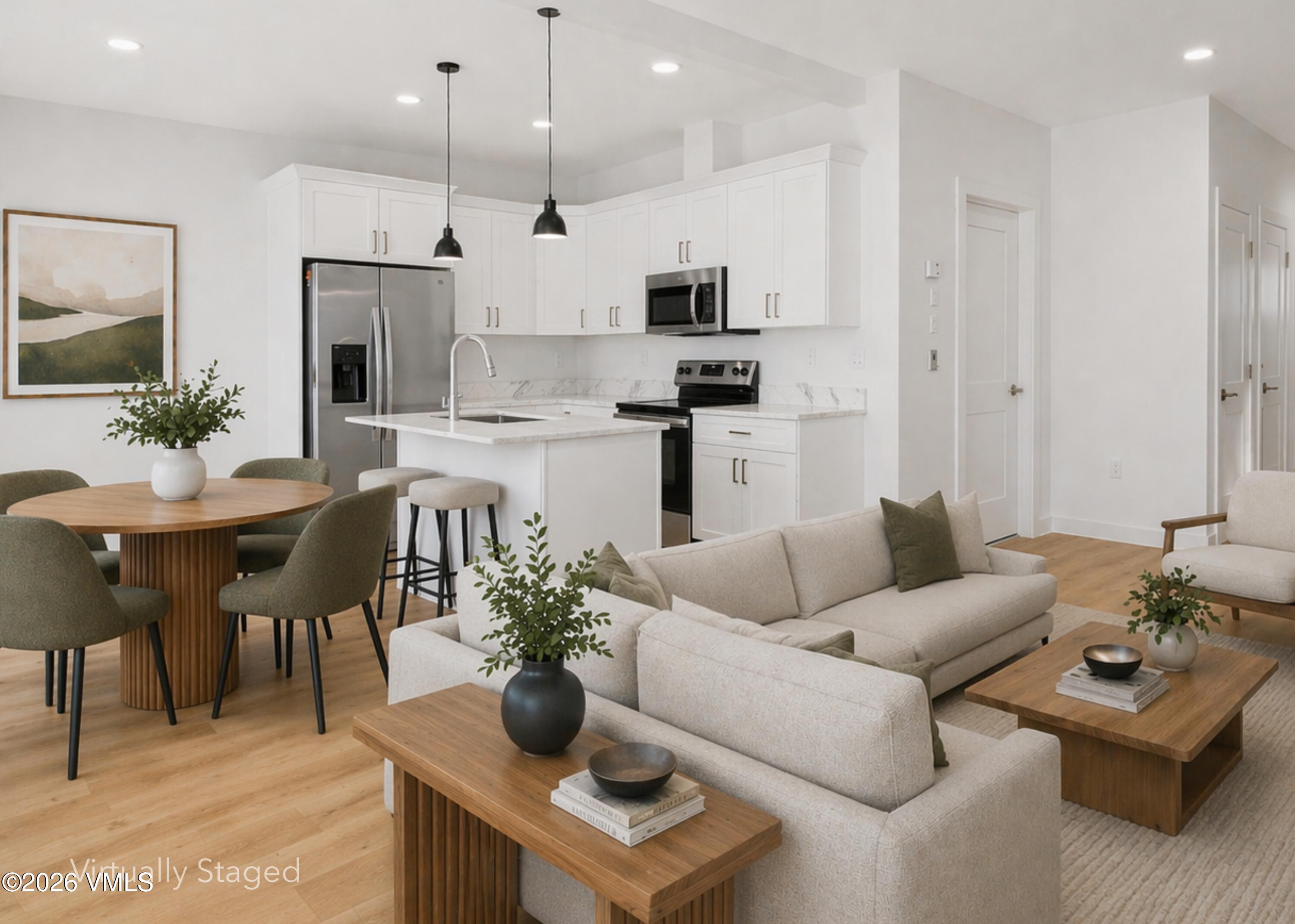 Open-plan kitchen and living room with white cabinets, stainless appliances, and virtually staged neutral furnishings.
