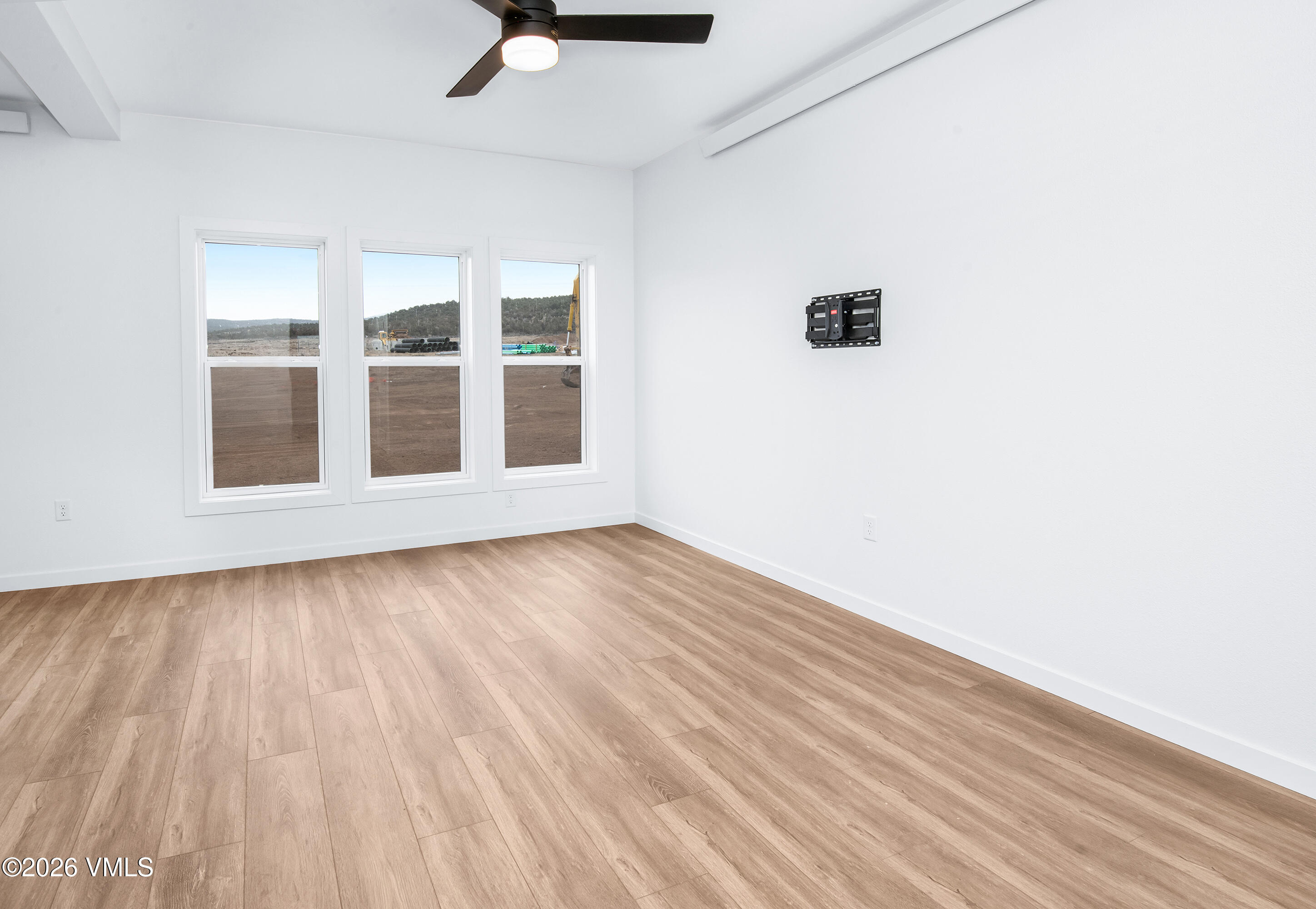 Empty room with light wood-look flooring, three windows, and a ceiling fan.