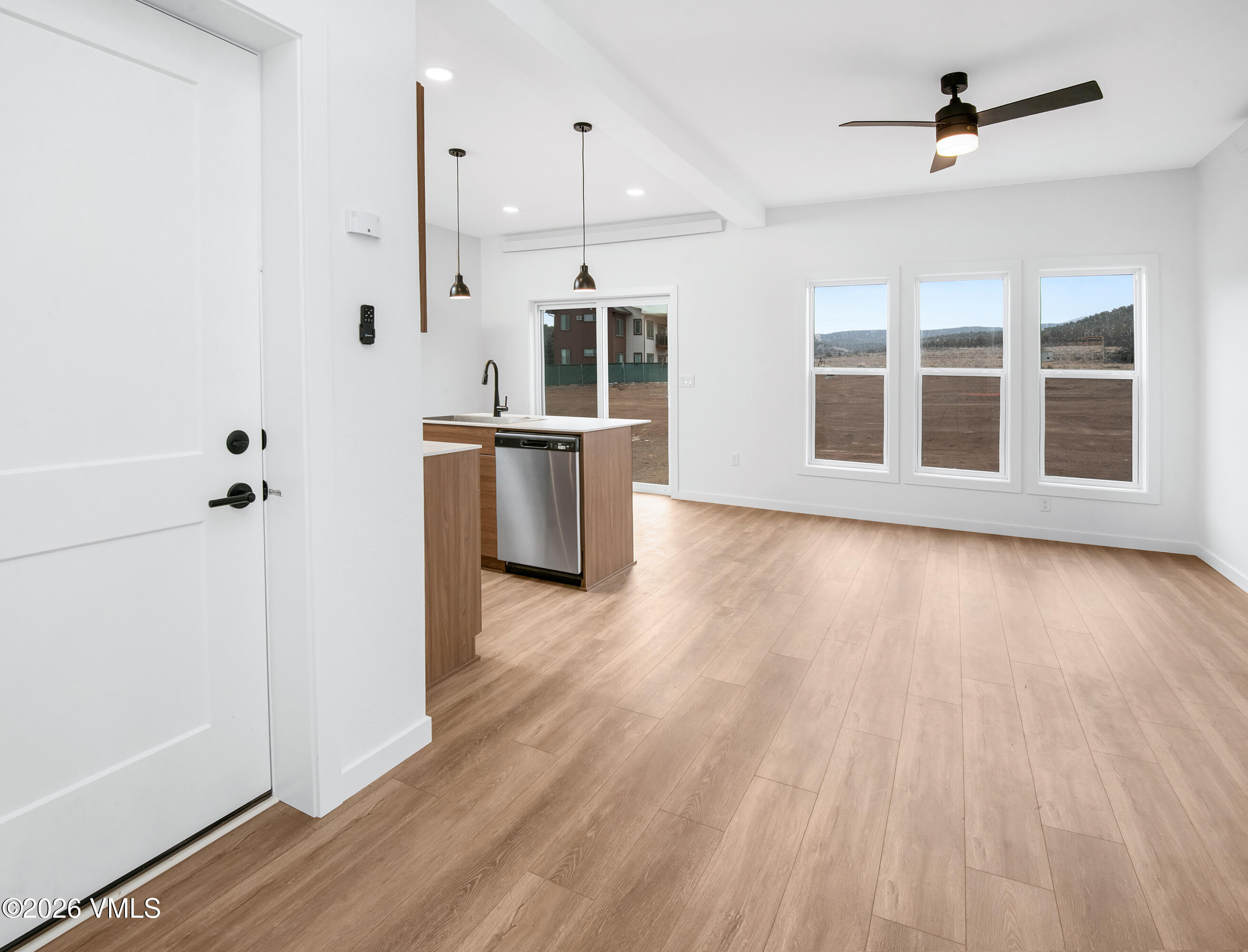 Vacant open-plan kitchen and living area with wood-look floors, island, and tall windows overlooking open land.