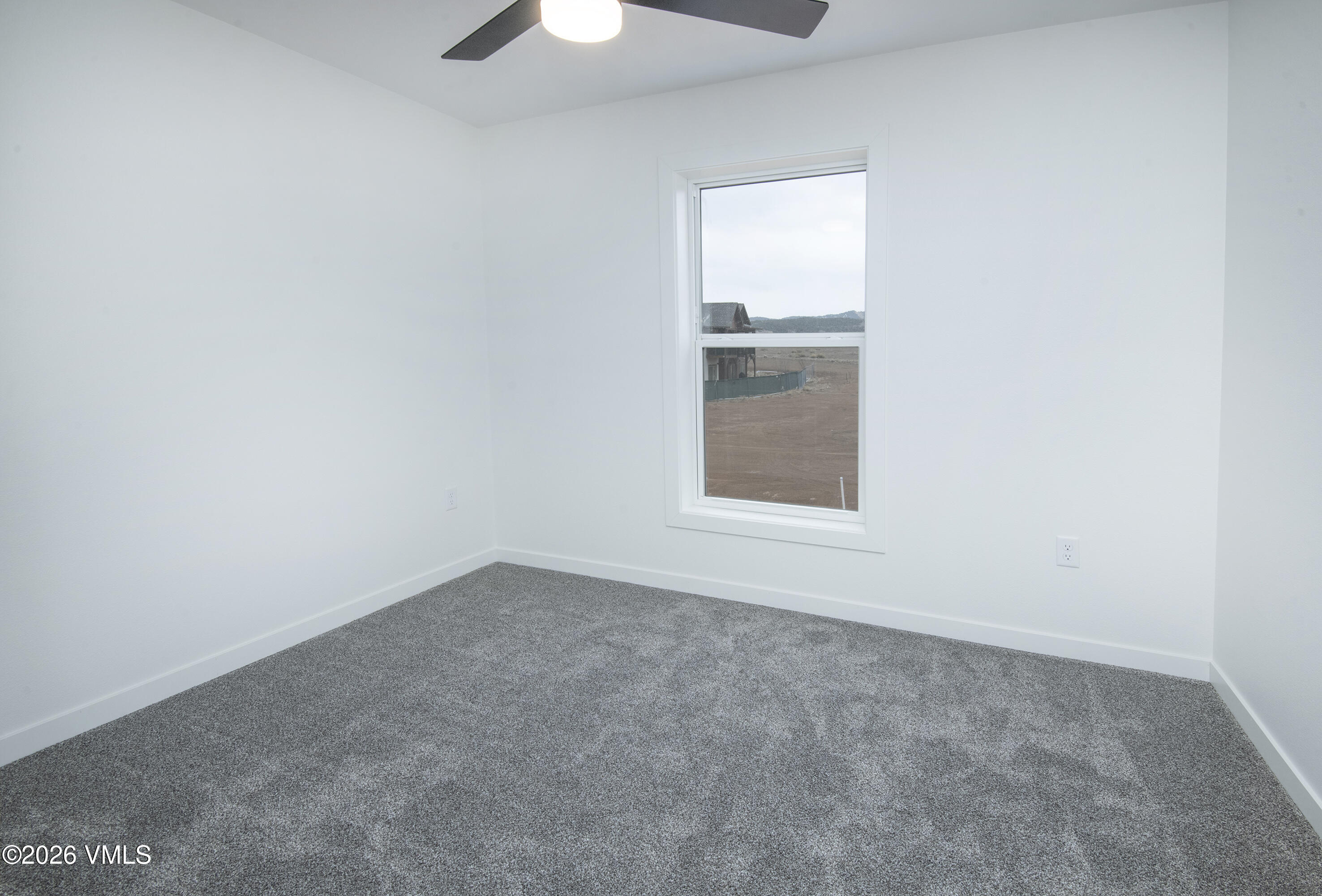 Empty bedroom with gray carpet, ceiling fan, and a window overlooking distant mountains.