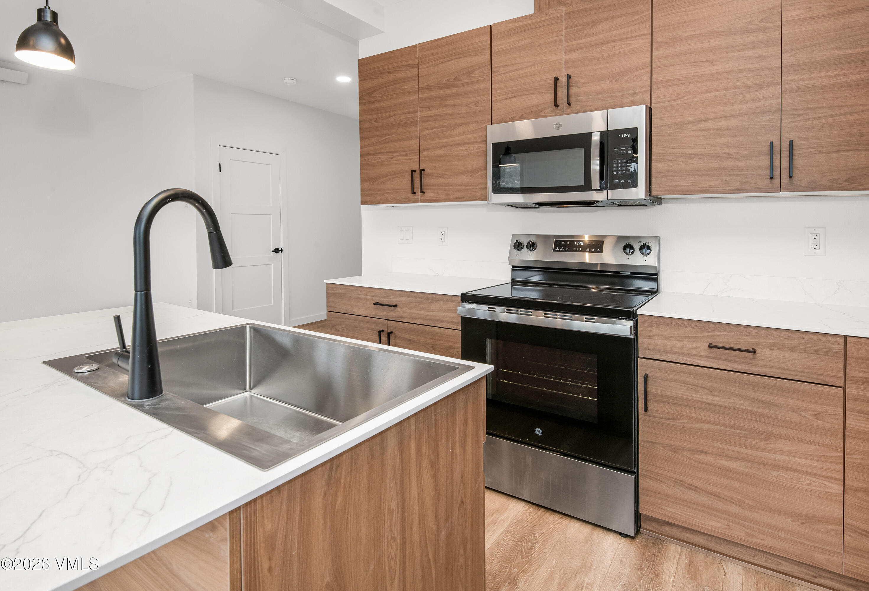 Modern kitchen with wood cabinets, white countertops, a large island sink, and stainless-steel appliances.