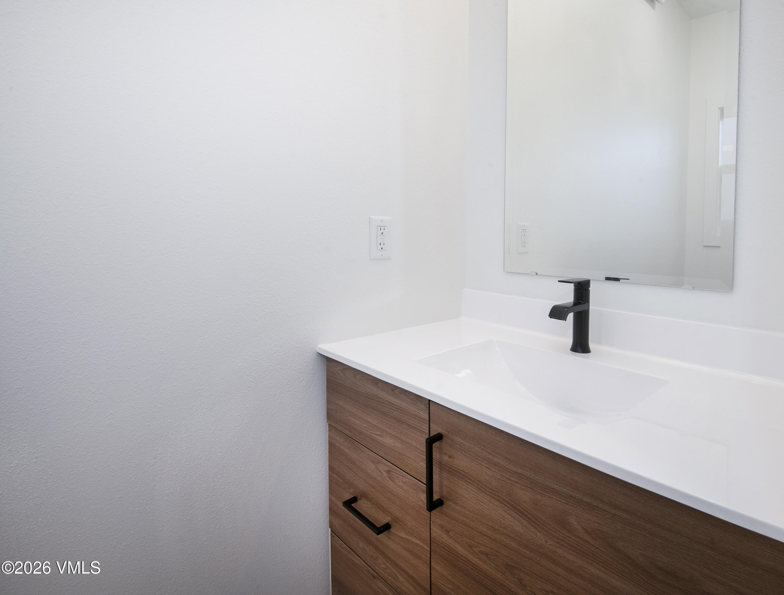 Bathroom vanity with a white sink, matte black faucet, and wood-grain drawers.