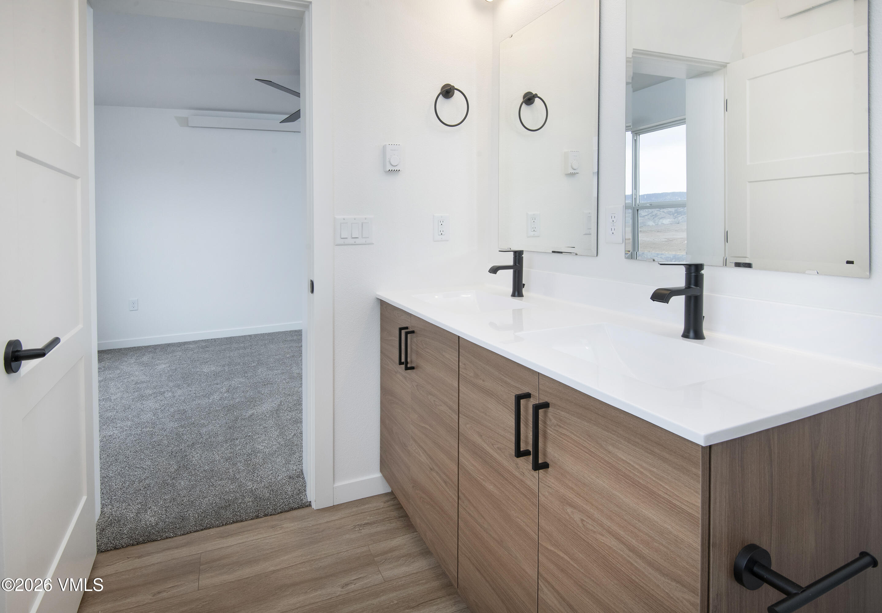 Bathroom with a double-sink wood vanity, white countertop, black faucets, and large mirrors.