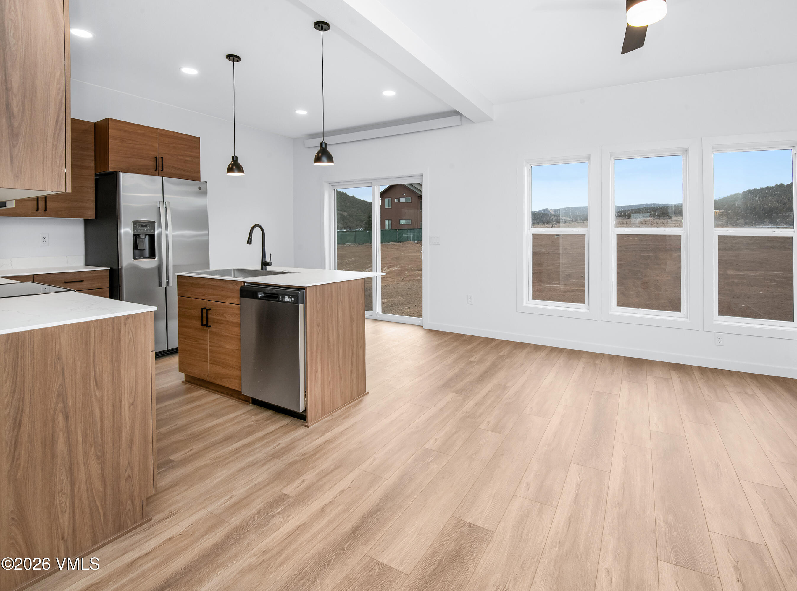 Vacant kitchen and dining area with wood cabinetry, a central island, and large windows overlooking wooded hills.