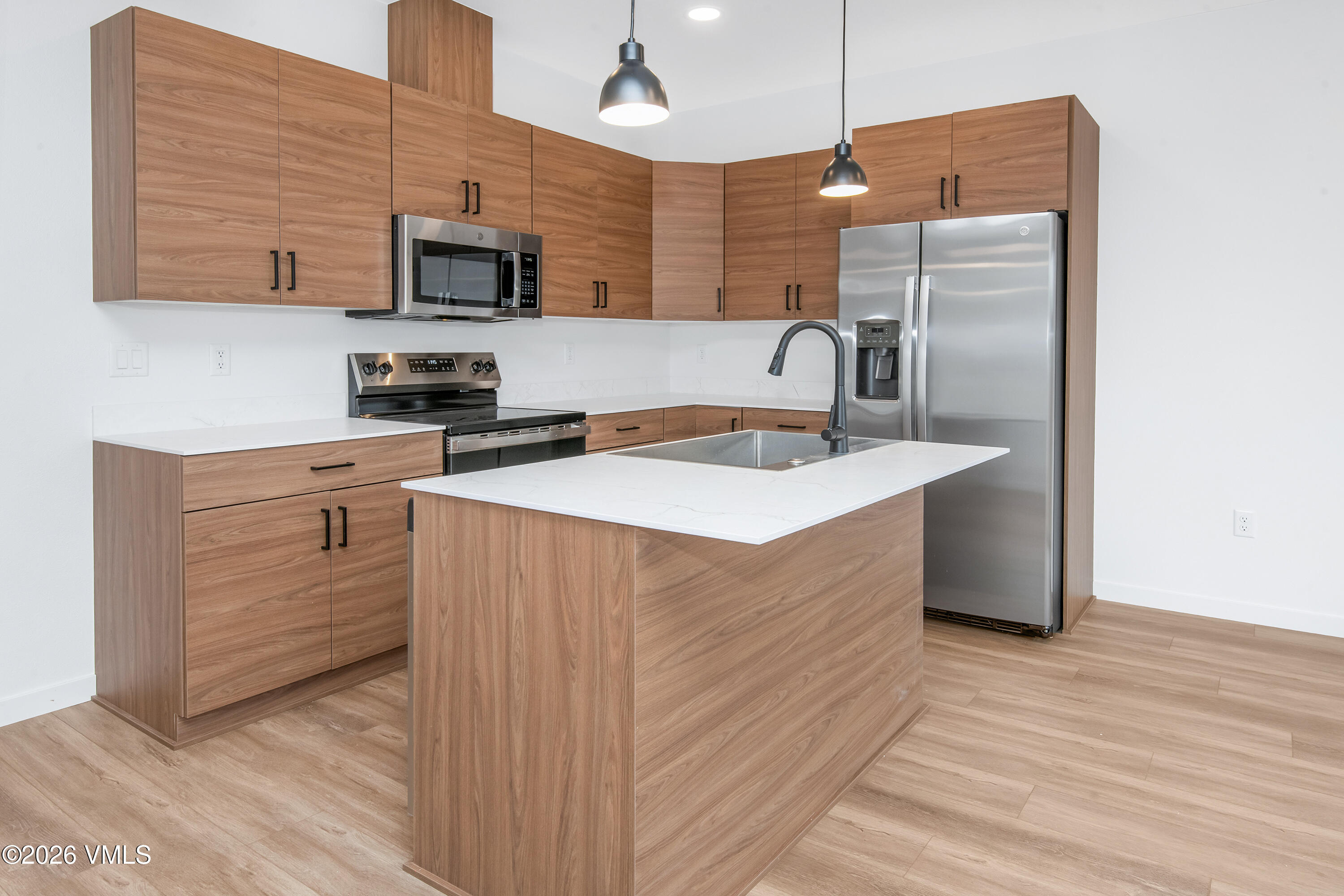 Modern kitchen with warm wood cabinets, a large island sink, and stainless steel appliances.