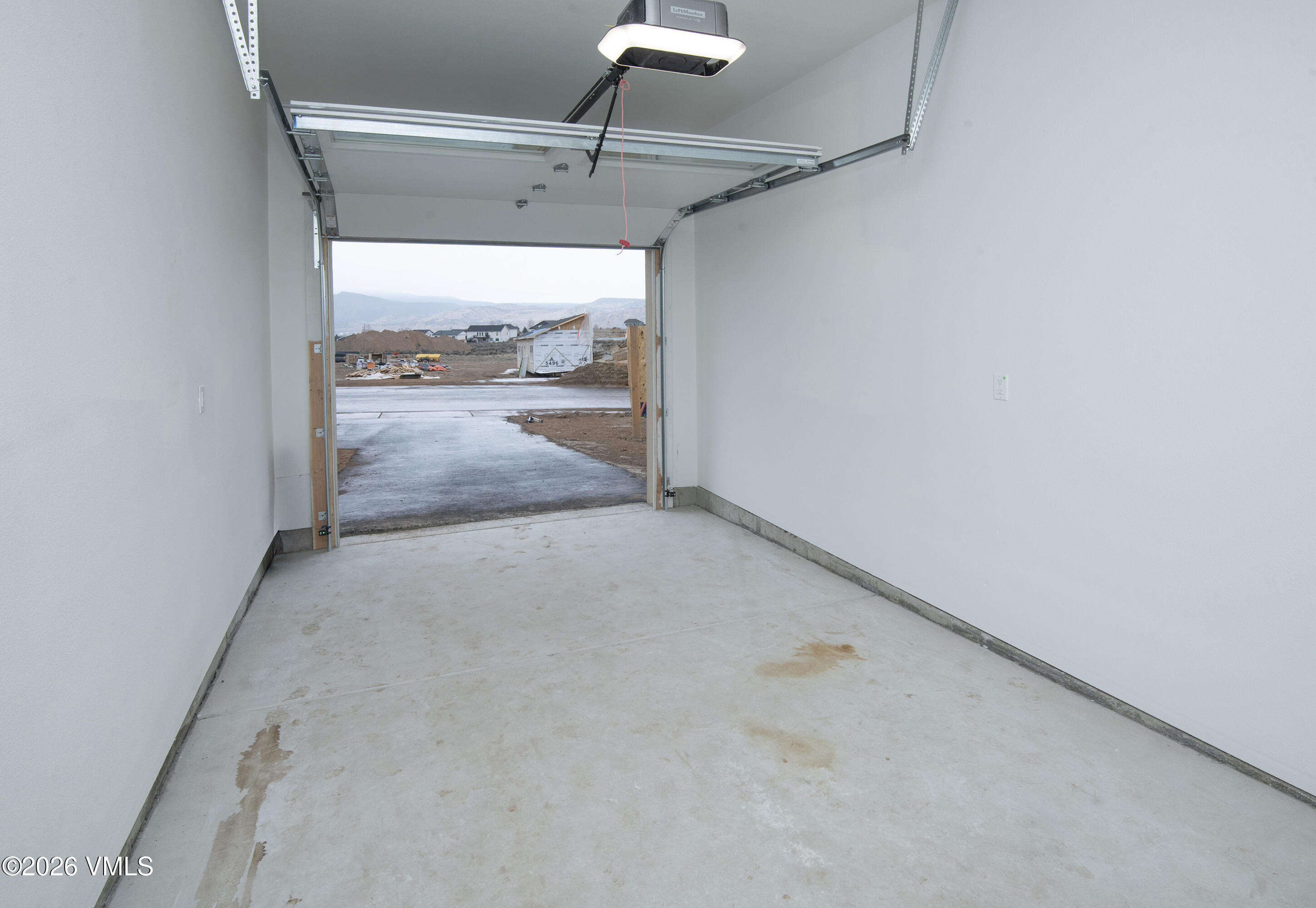 Empty garage with open overhead door, concrete floor, and a construction site visible outside.