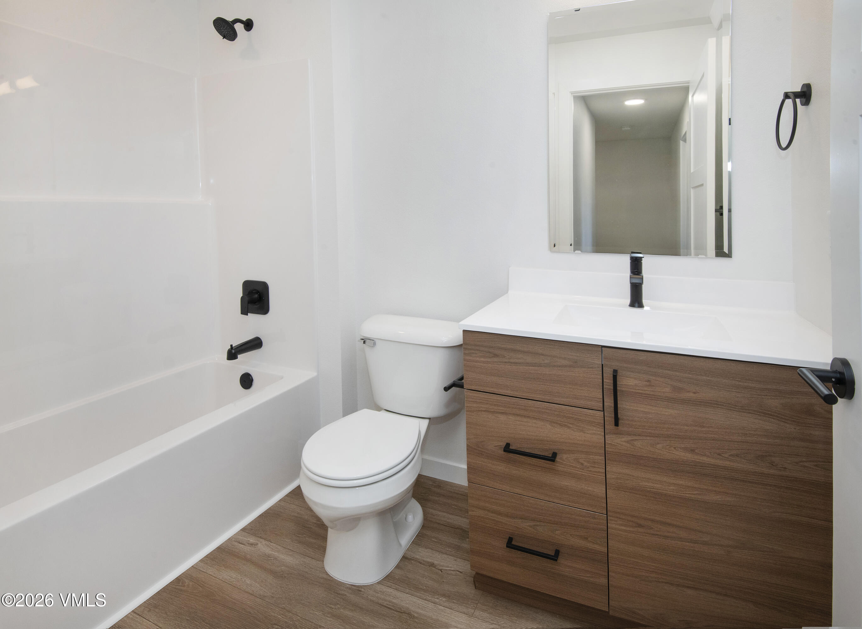 Modern bathroom with a white tub, wood-grain vanity, and matte-black fixtures.