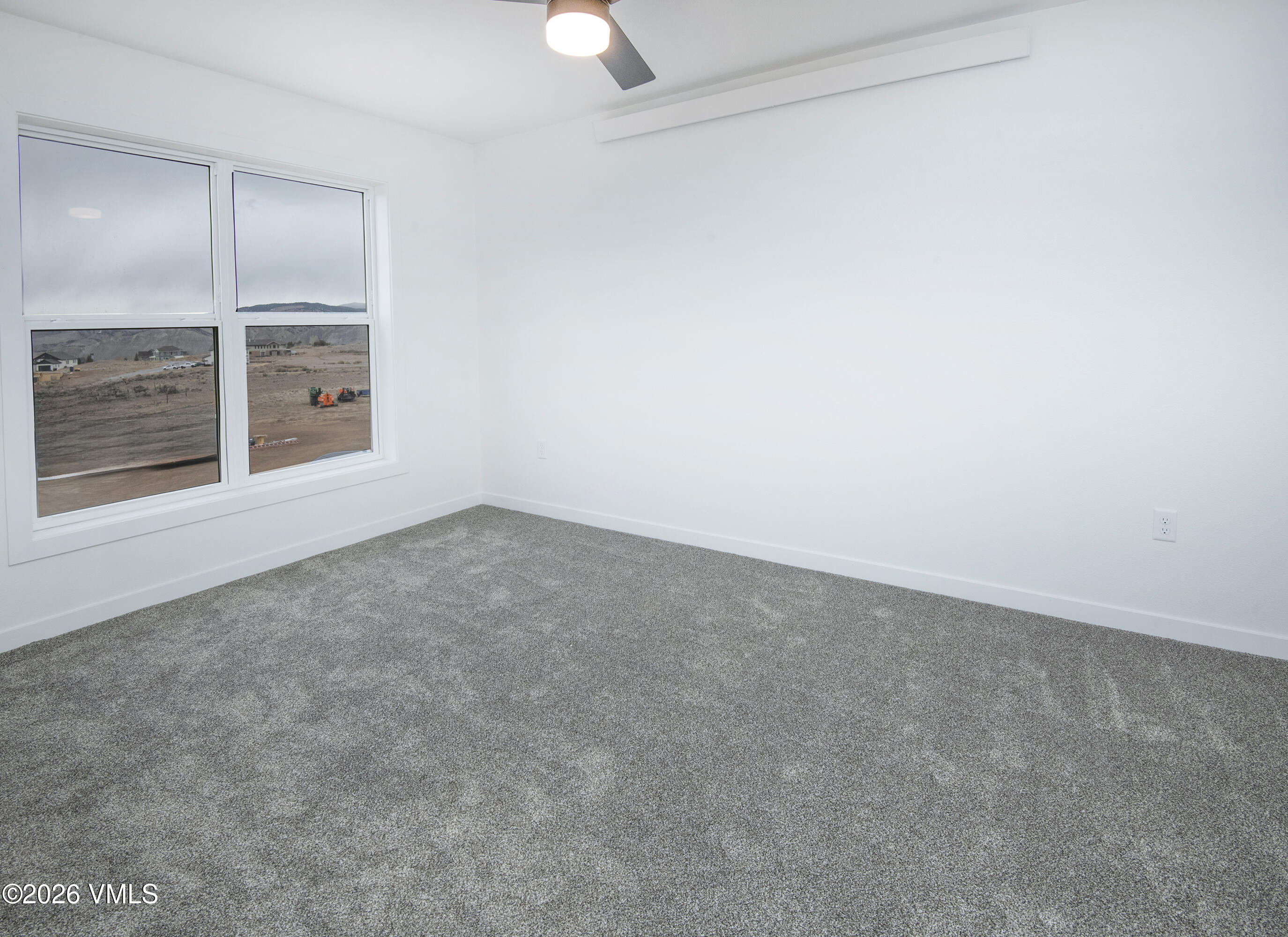 Unfurnished carpeted room with two large windows overlooking open land and low hills.