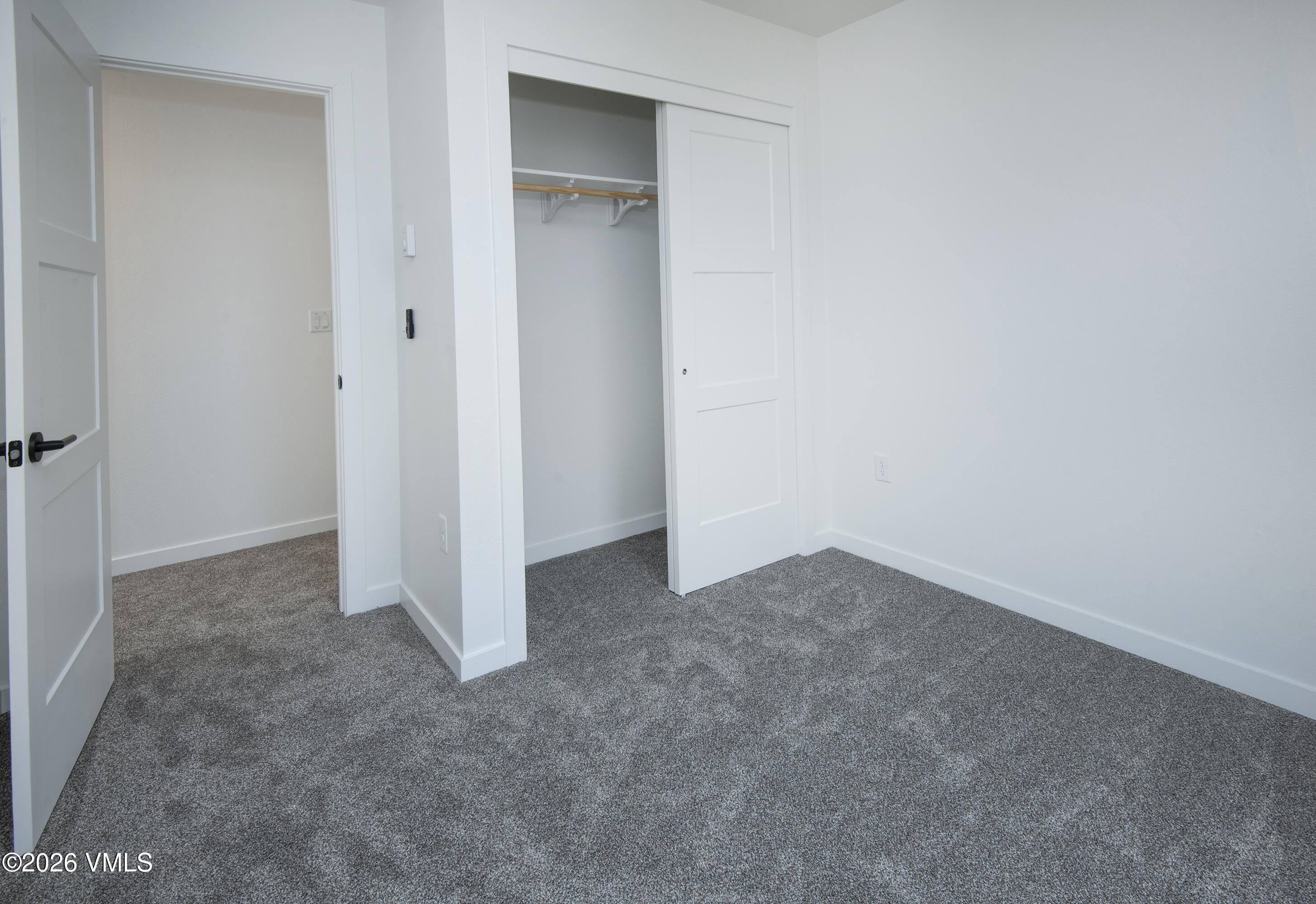 Empty bedroom with gray carpet and an open closet with a hanging rod.